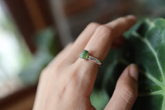 Green Tourmaline ring shown worn on a hand against leaves, with polished silver and deep green crystal detail.