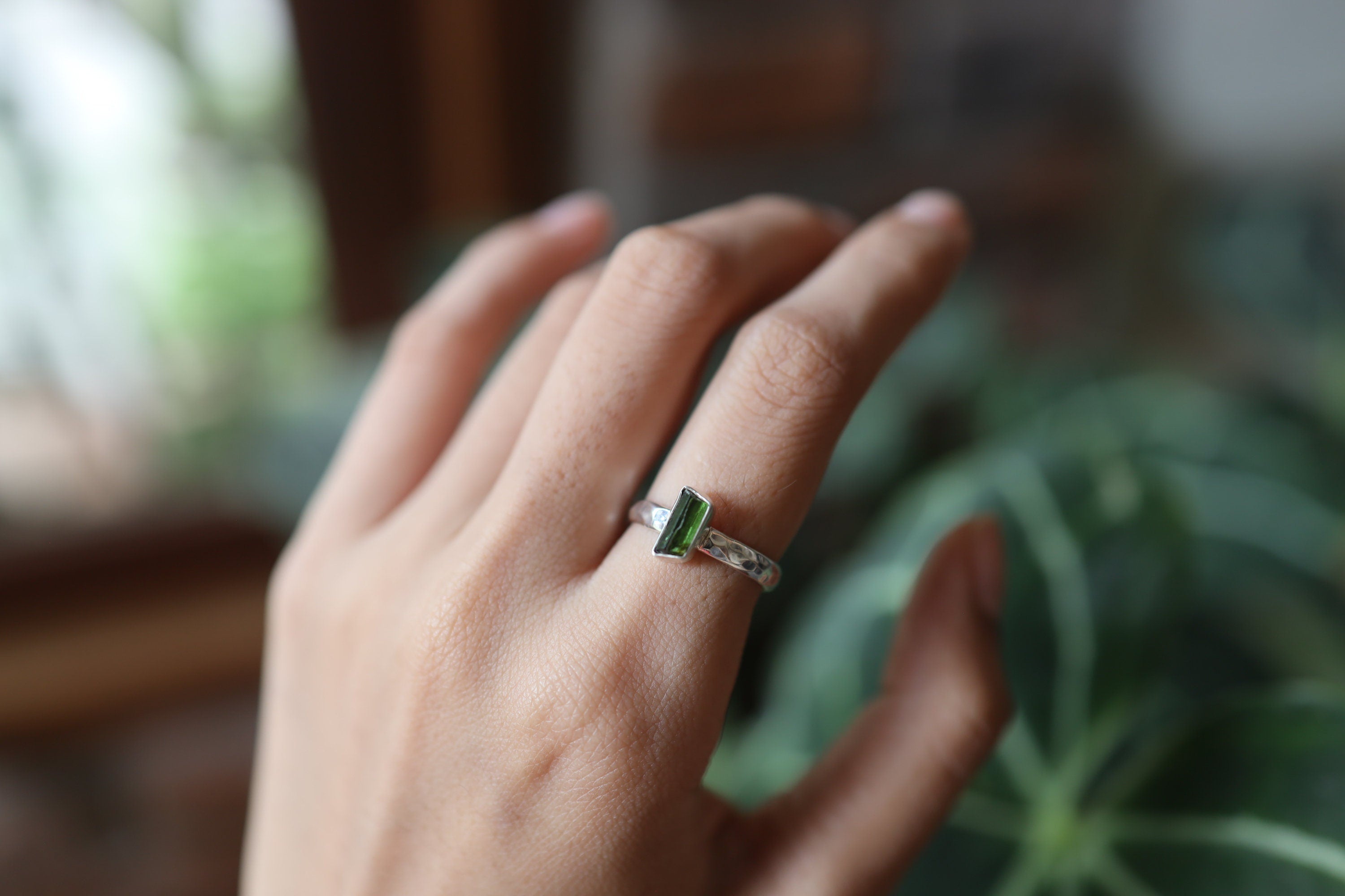 Green Tourmaline ring shown worn on a hand against leaves, with polished silver and deep green crystal detail.