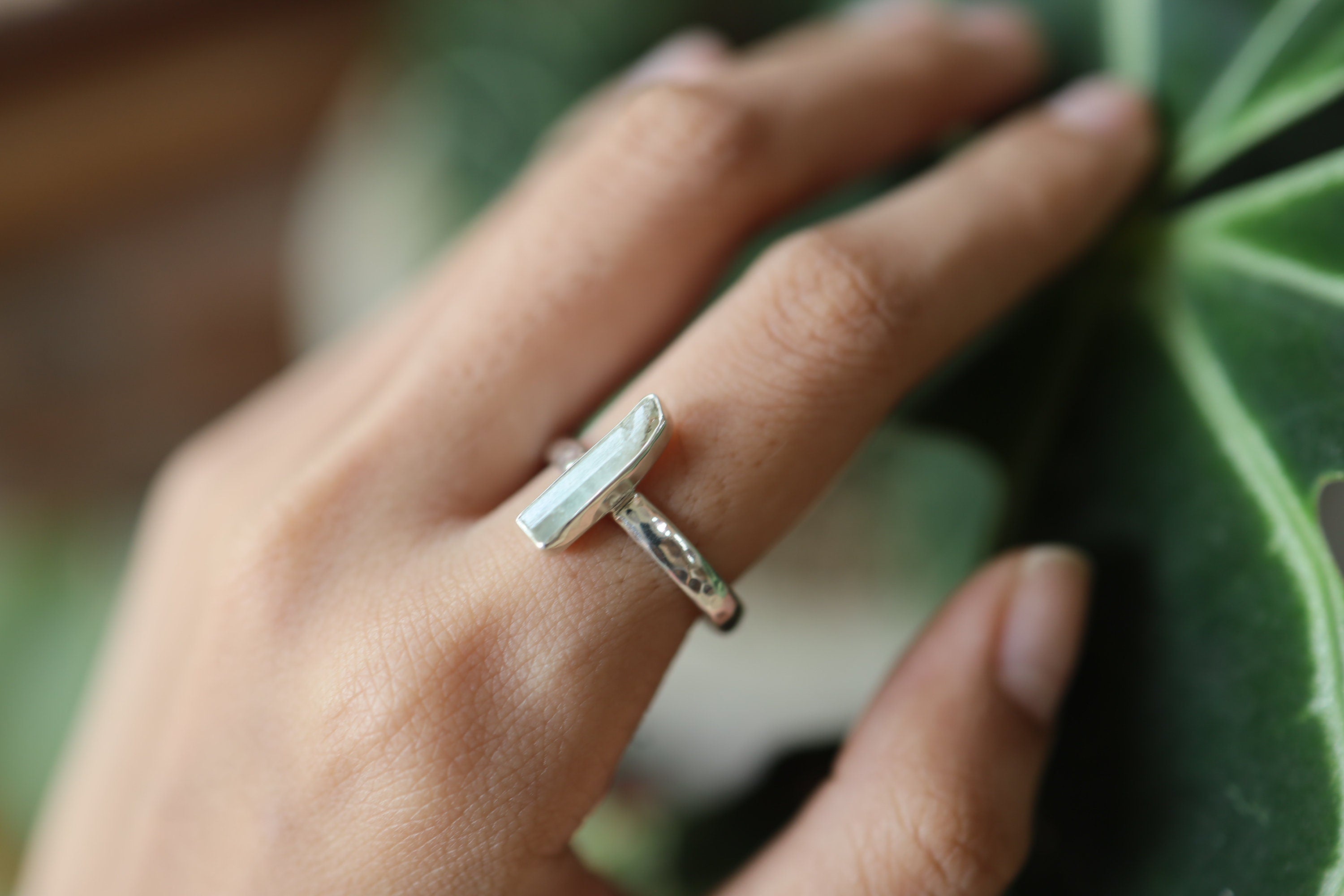 Long Aquamarine ring shown worn on a hand against green leaves, with ocean-blue stone and handmade silver setting.