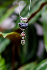 Mount Darwin Tektite Watermelon Tourmaline Pyrite pendant shown outdoors, with raw stones in a vertical sterling silver layout.