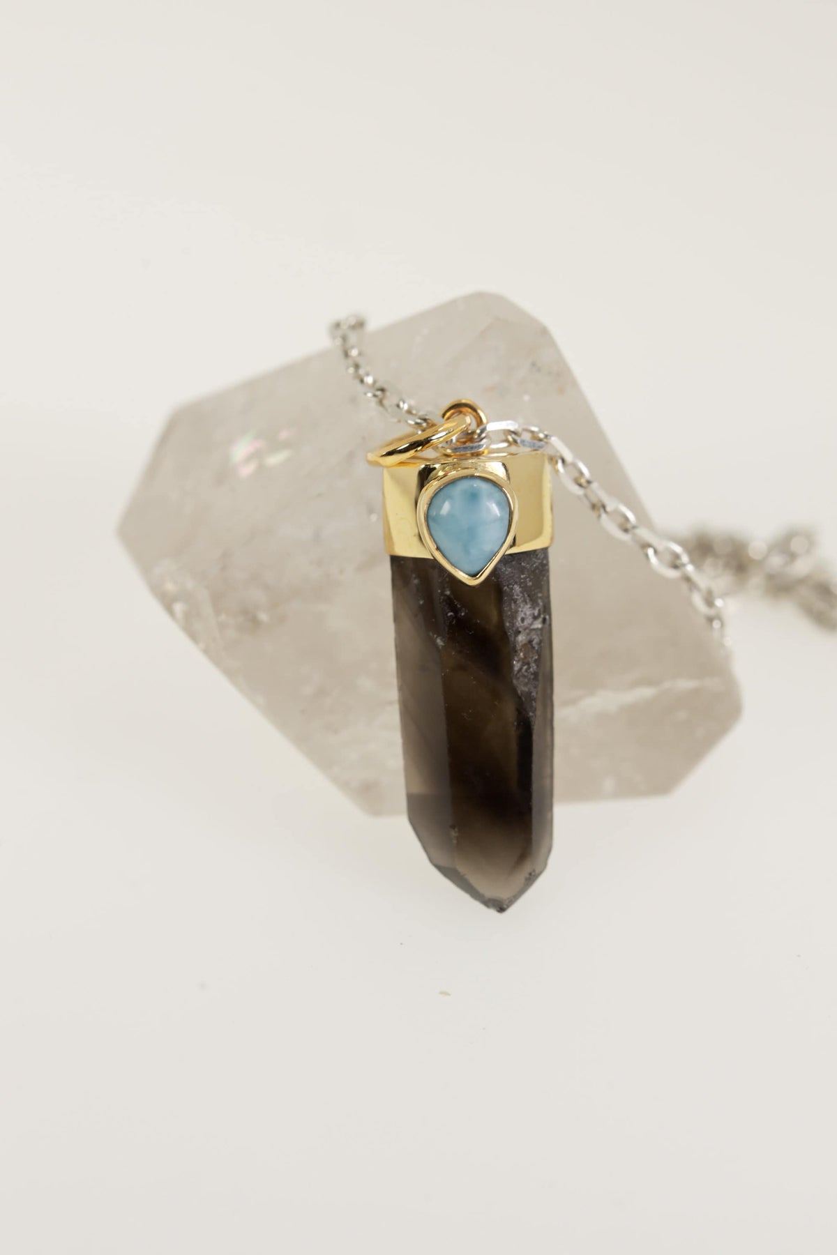 Smoky Phantom Quartz Larimar pendant displayed on Clear Quartz with gold-plated sterling silver cap and blue cabochon.