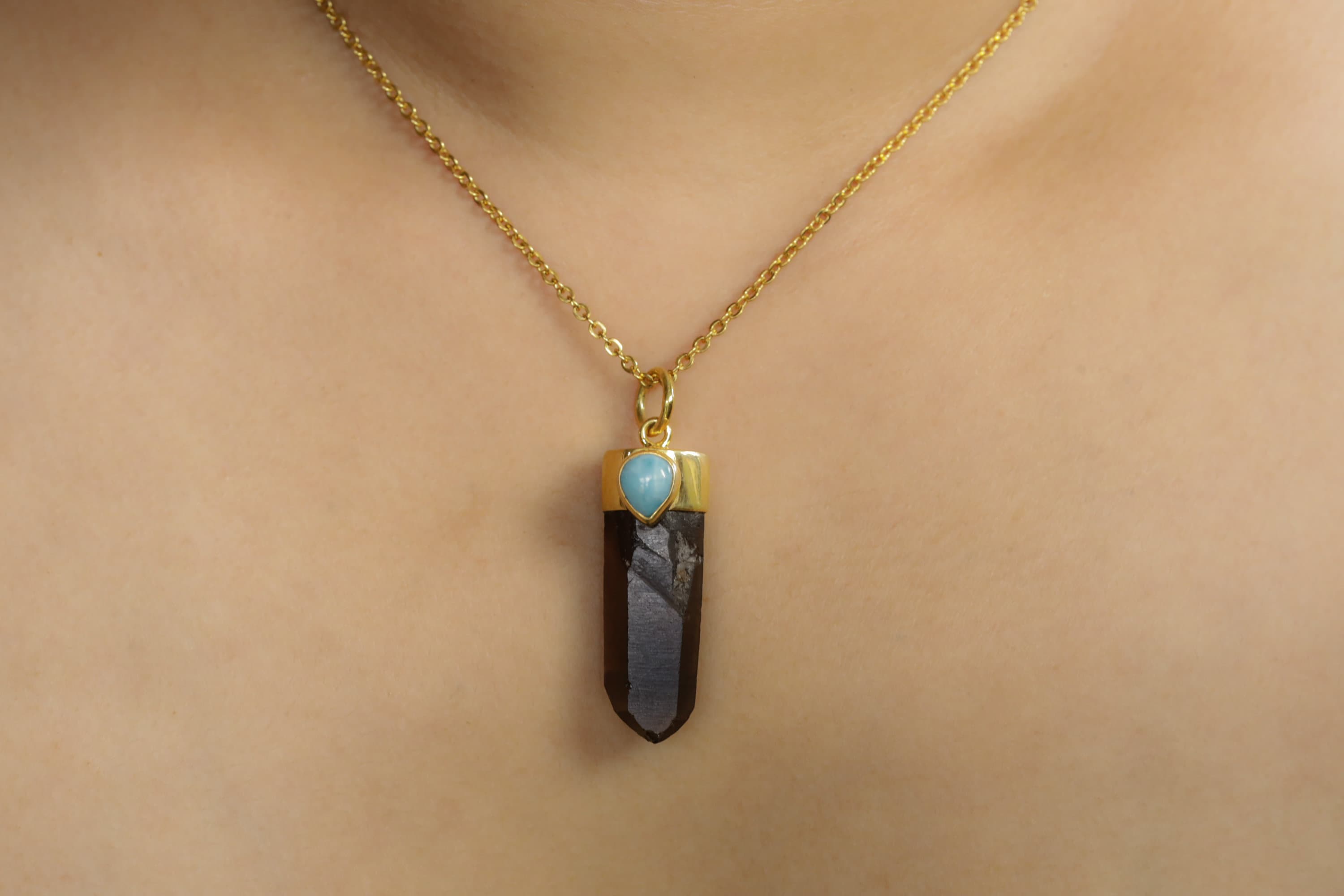 Smoky Phantom Quartz Larimar pendant worn on a model with gold chain and ocean-blue cabochon detail.
