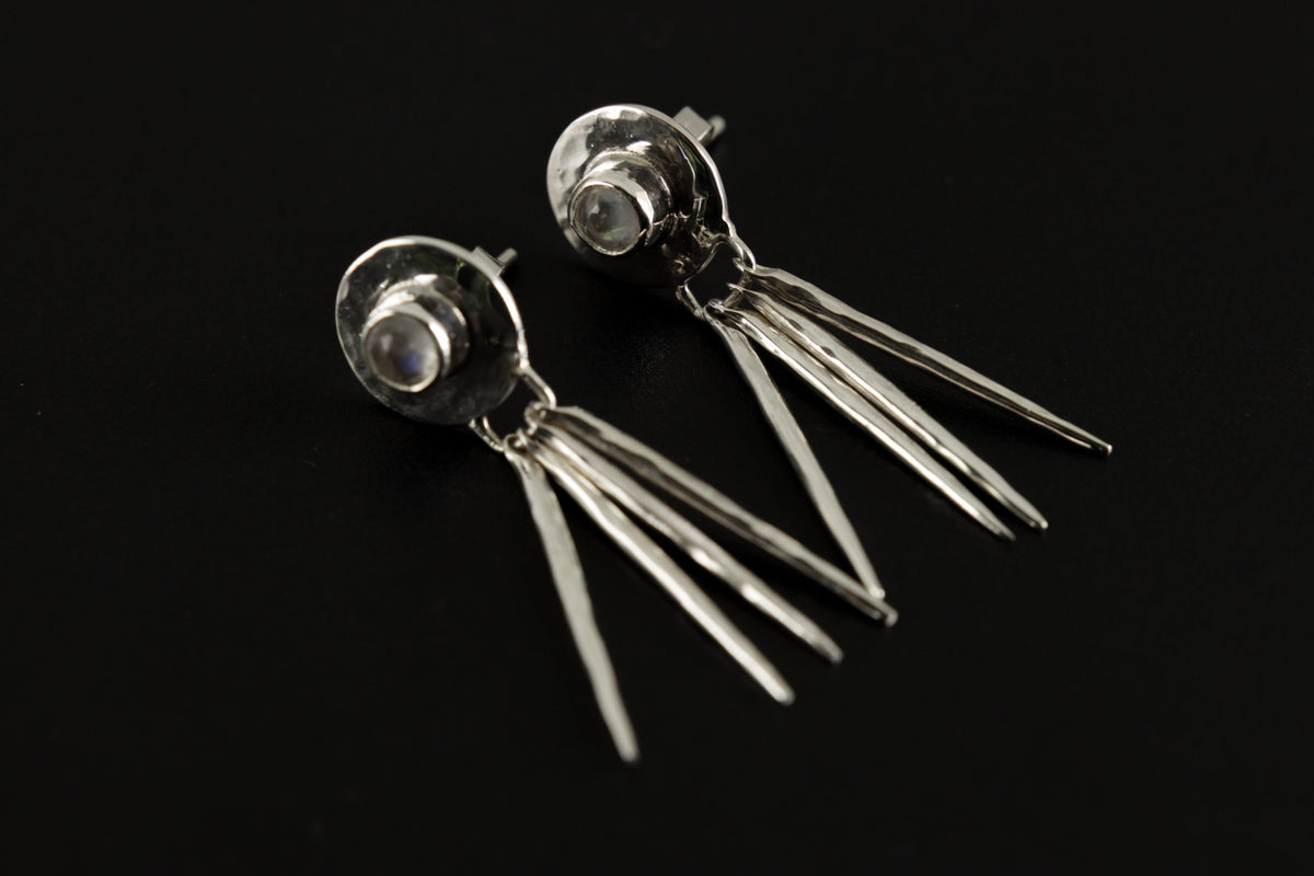 Handmade 925 sterling silver Blue Moonstone drop earrings shown on a dark background, with hammered circle settings and silver stick dangles.