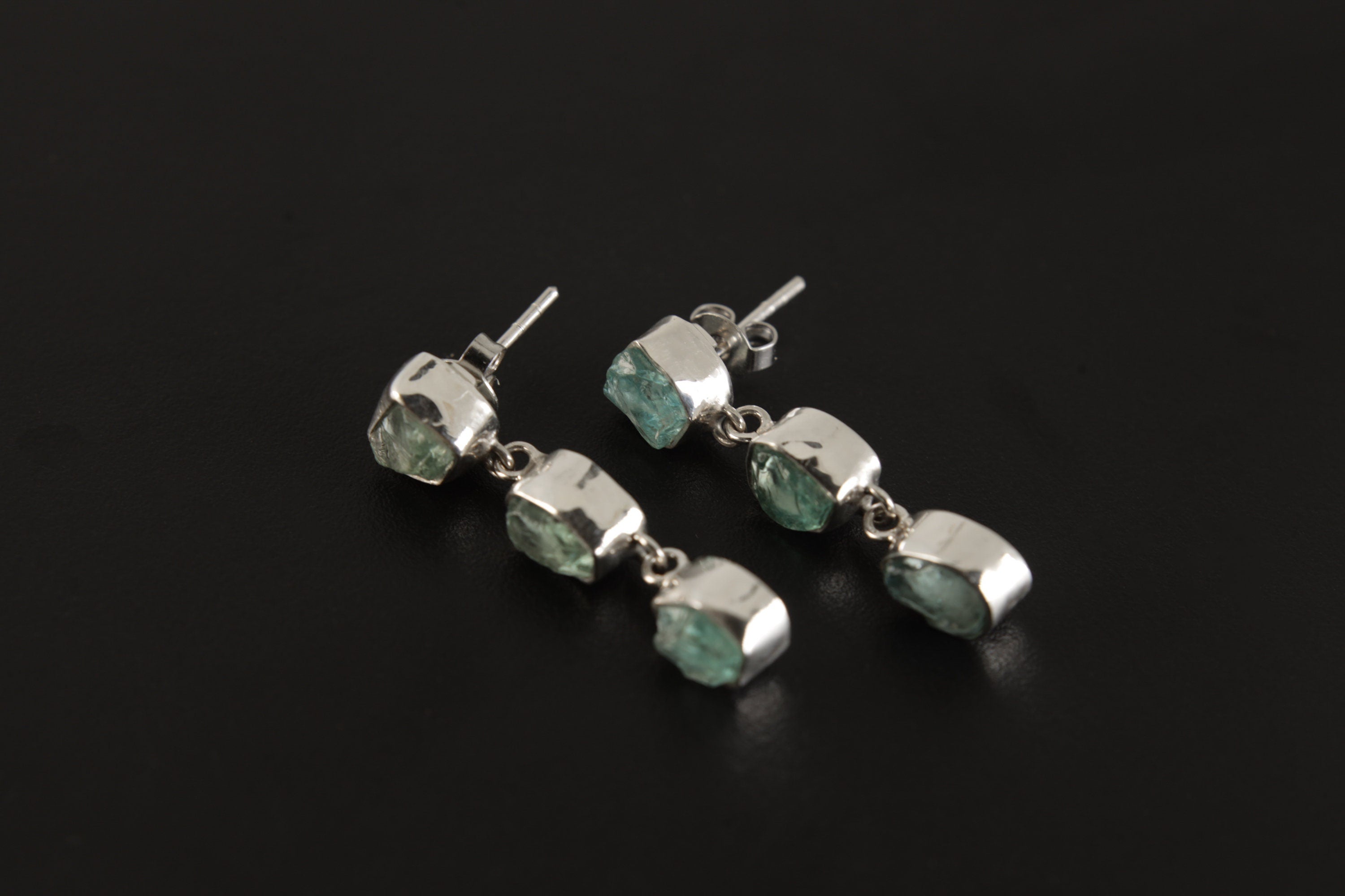 Blue Apatite geometric earrings displayed on a dark background, with three-stone sterling silver drop design.