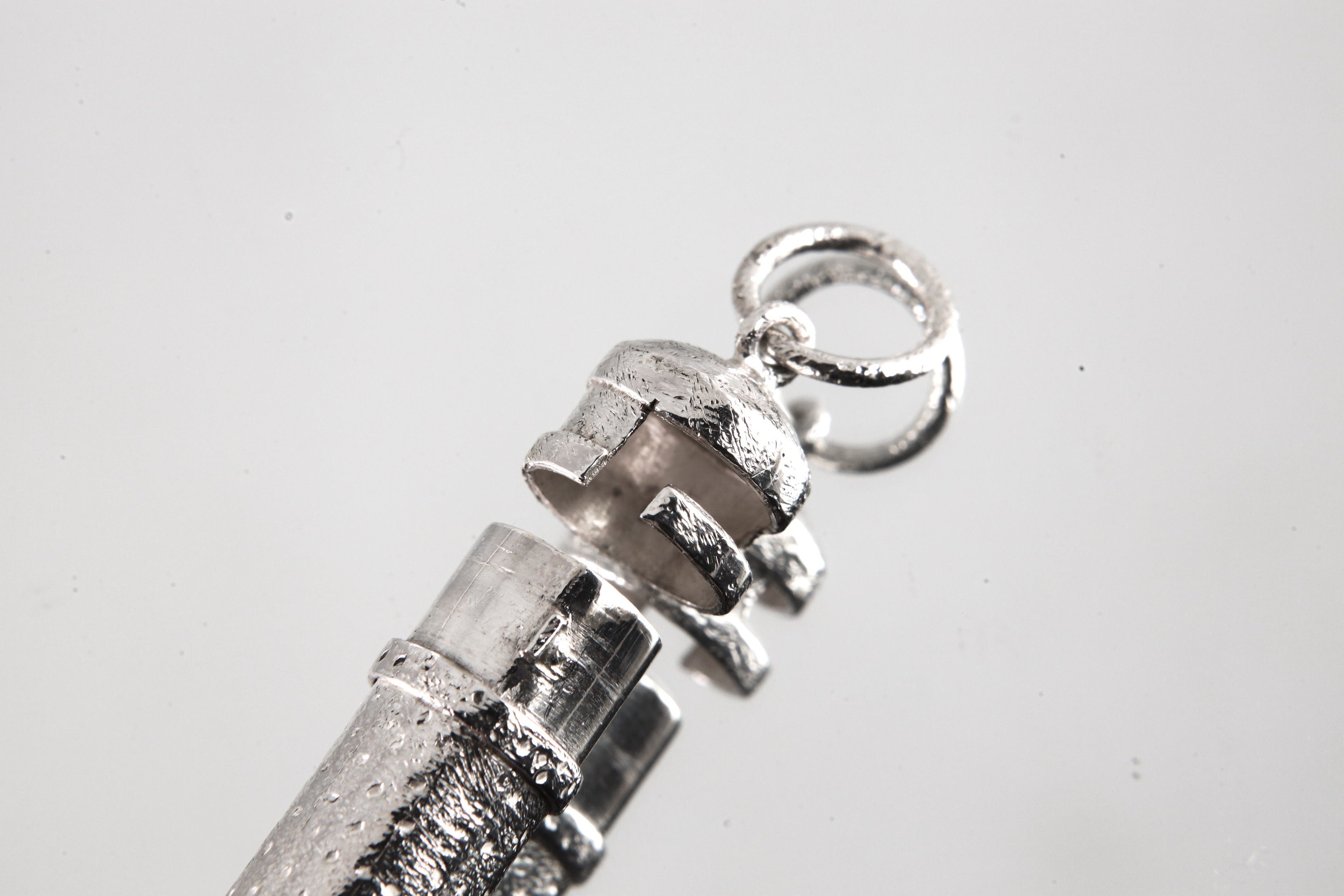 Close-up of sterling silver capsule pendant showing sand-textured surface, round bail, and opening mechanism.
