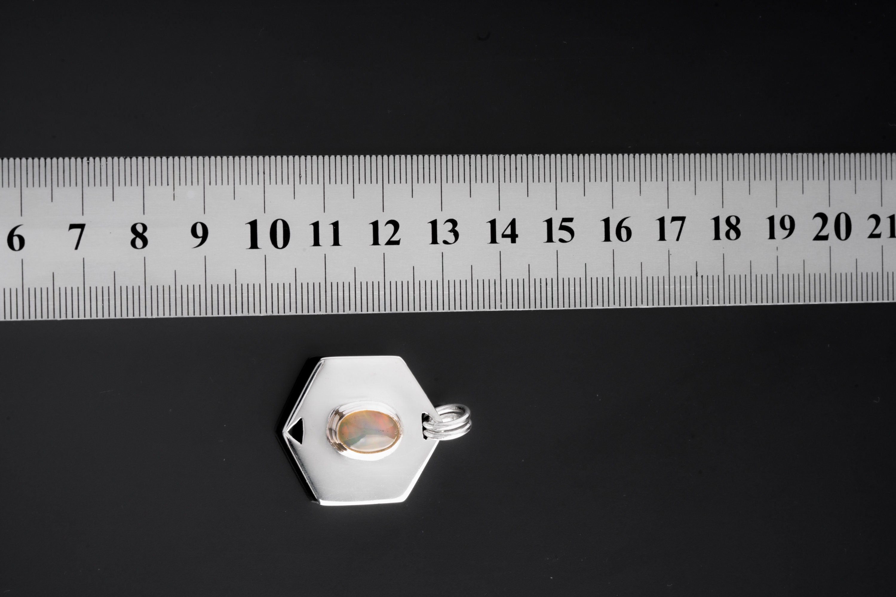 Ethiopian Opal hexagon pendant shown beside a ruler for scale with polished sterling silver frame.