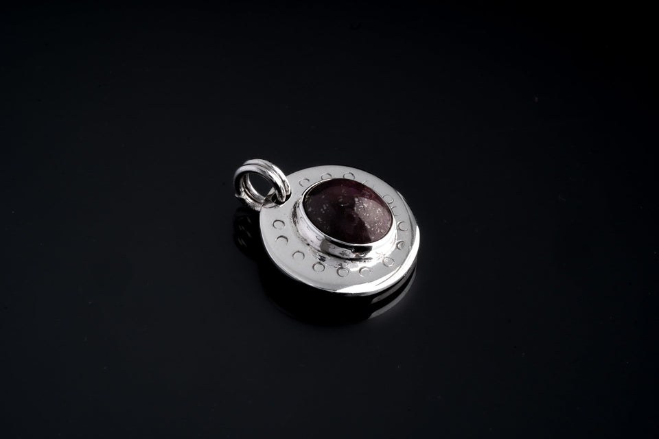 Close-up of Ruby Cabochon pendant on black background, showing polished sterling silver crescent texture and twin round bails.