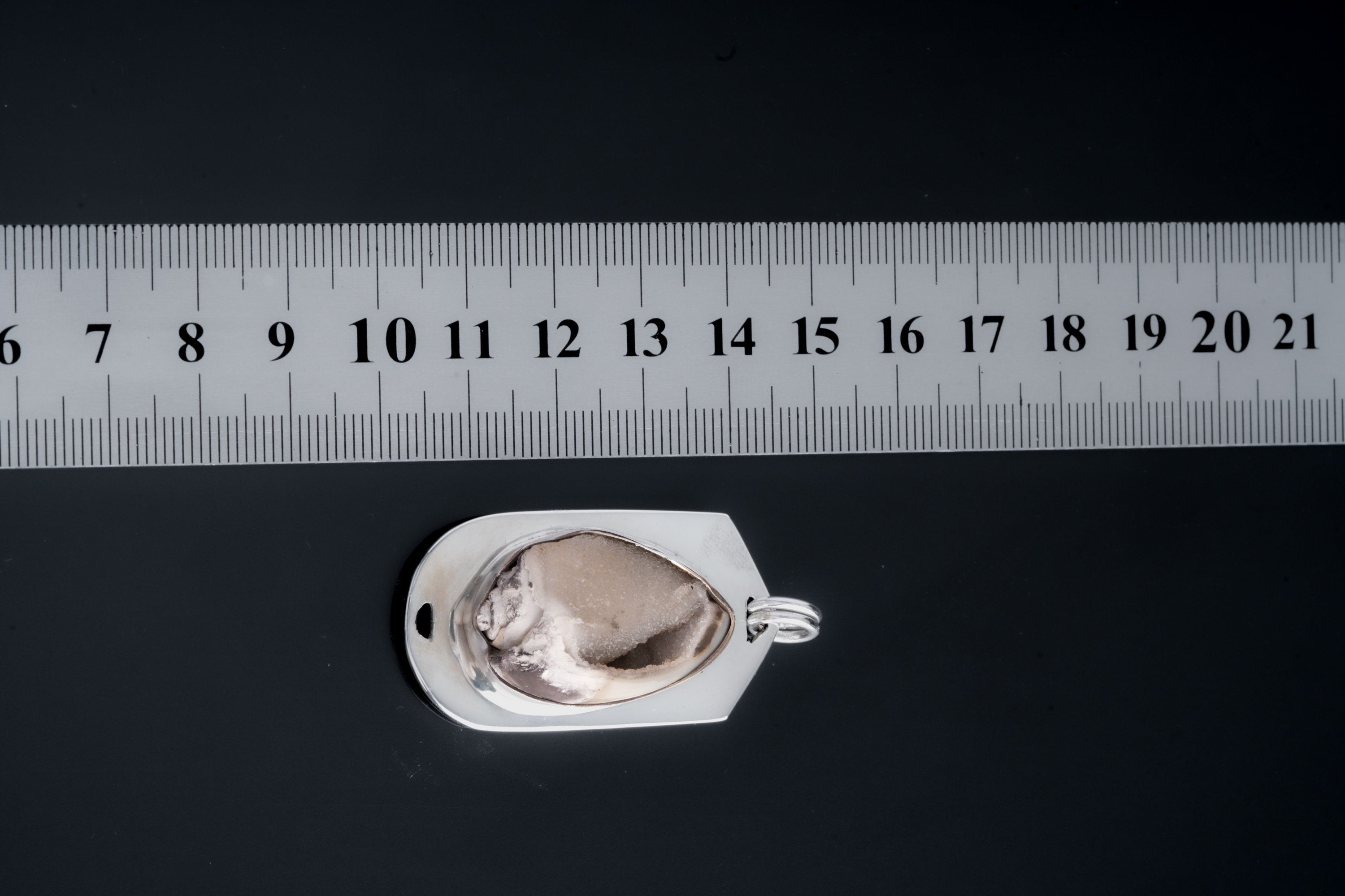 Fossilized Drusy Shell pendant shown beside a ruler for scale with polished sterling silver frame.