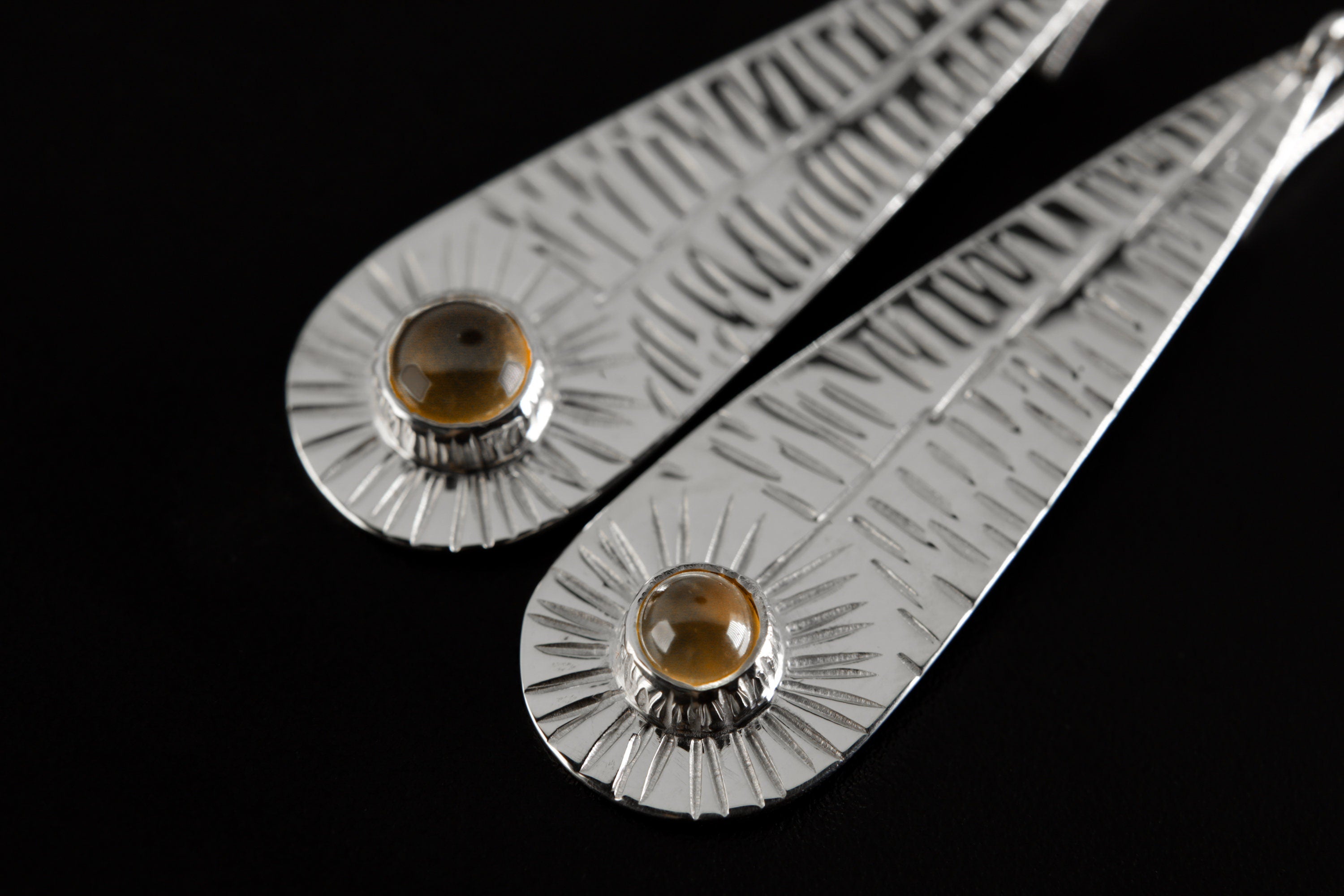 Close-up of handmade silver leaf earrings showing vein-like texture, polished sterling silver, and Orange Agate base stones.