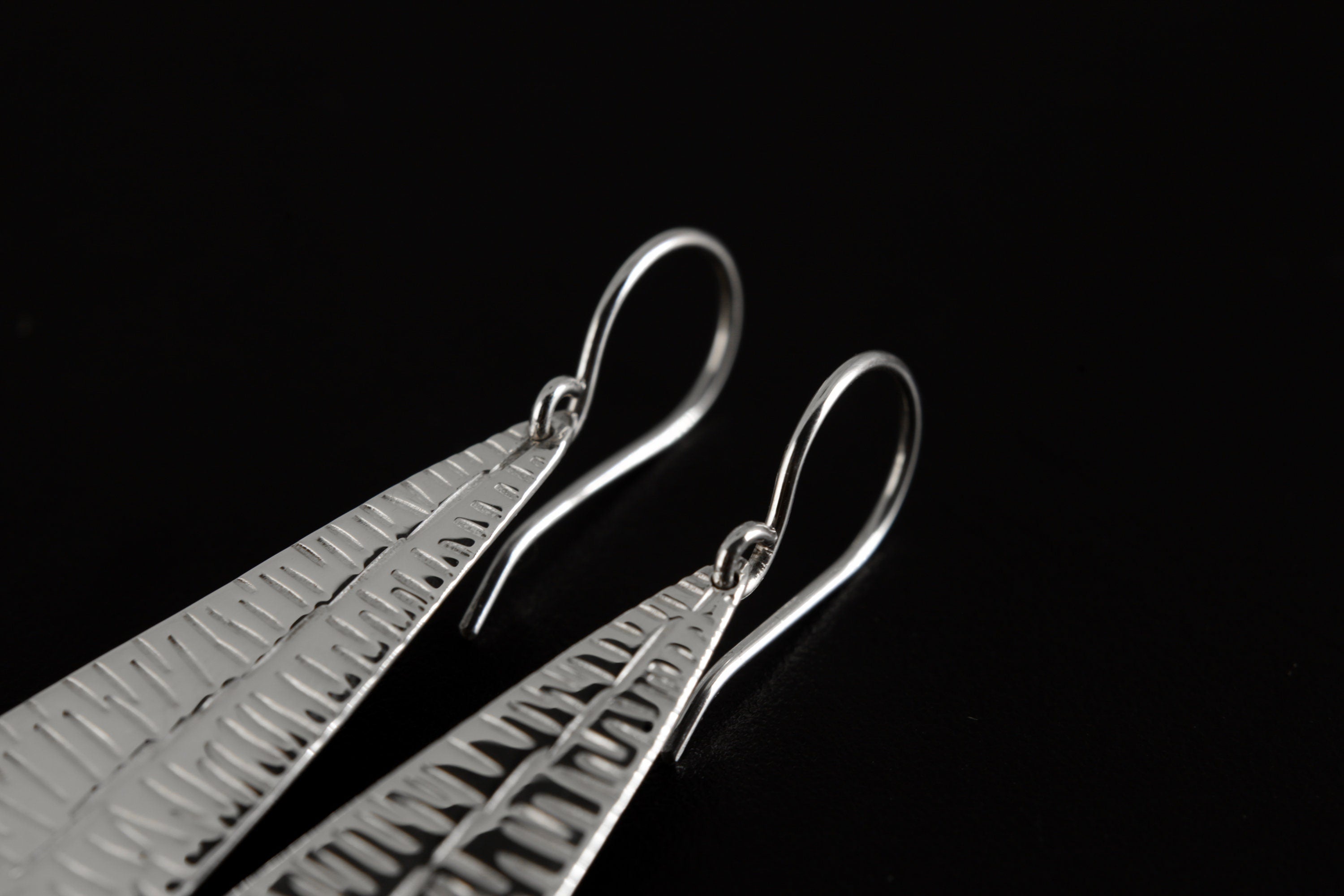 Close-up of handmade silver leaf earrings showing vein-like texture, polished sterling silver, and Orange Agate base stones.