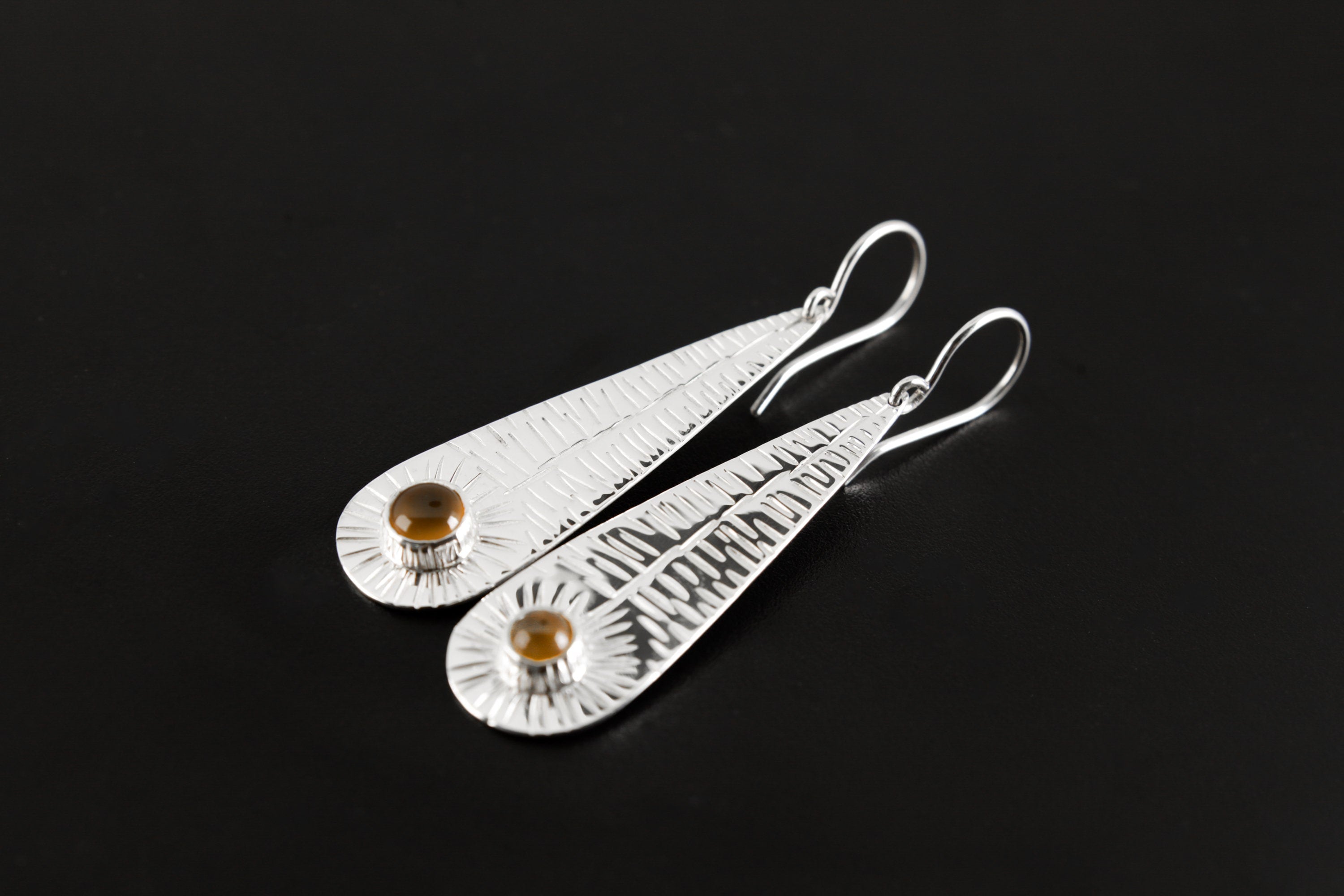 Leaf-shaped sterling silver earrings shown on a dark background with polished botanical texture and round Orange Agate stones.