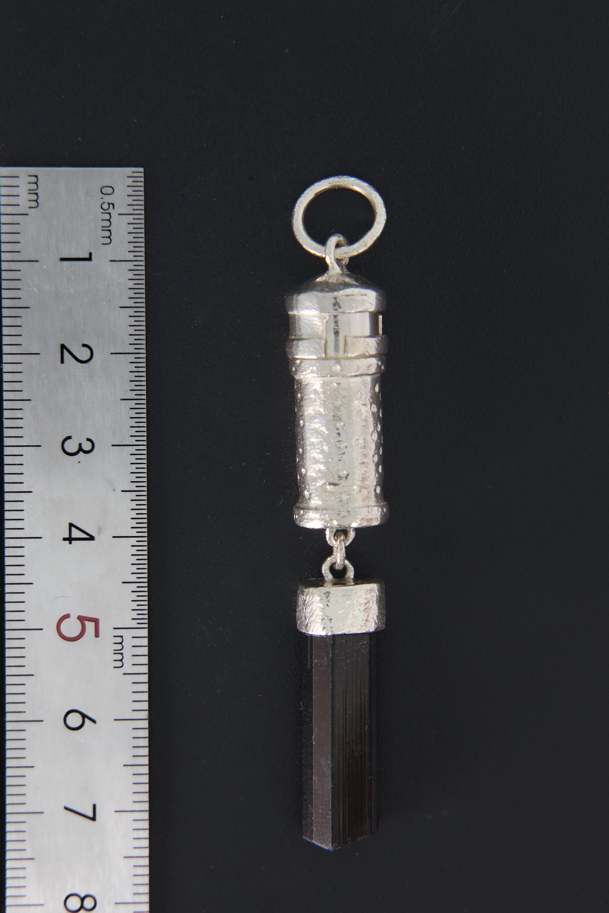 Black Tourmaline sterling silver capsule pendant shown beside a ruler for scale, with raw crystal base and round bail.