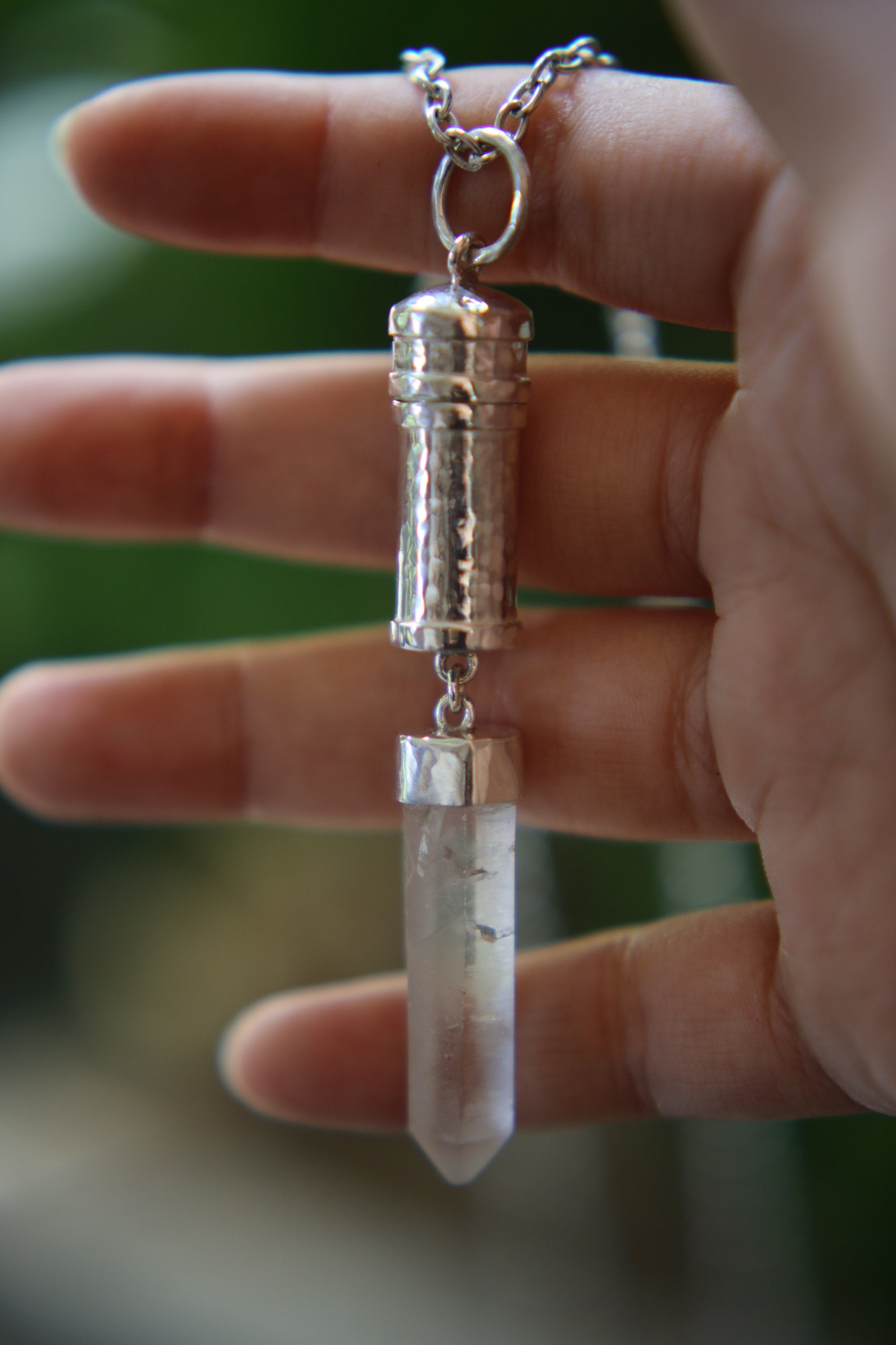 Australian Clear Quartz capsule pendant held in hand, showing hidden vessel form and polished silver detail.