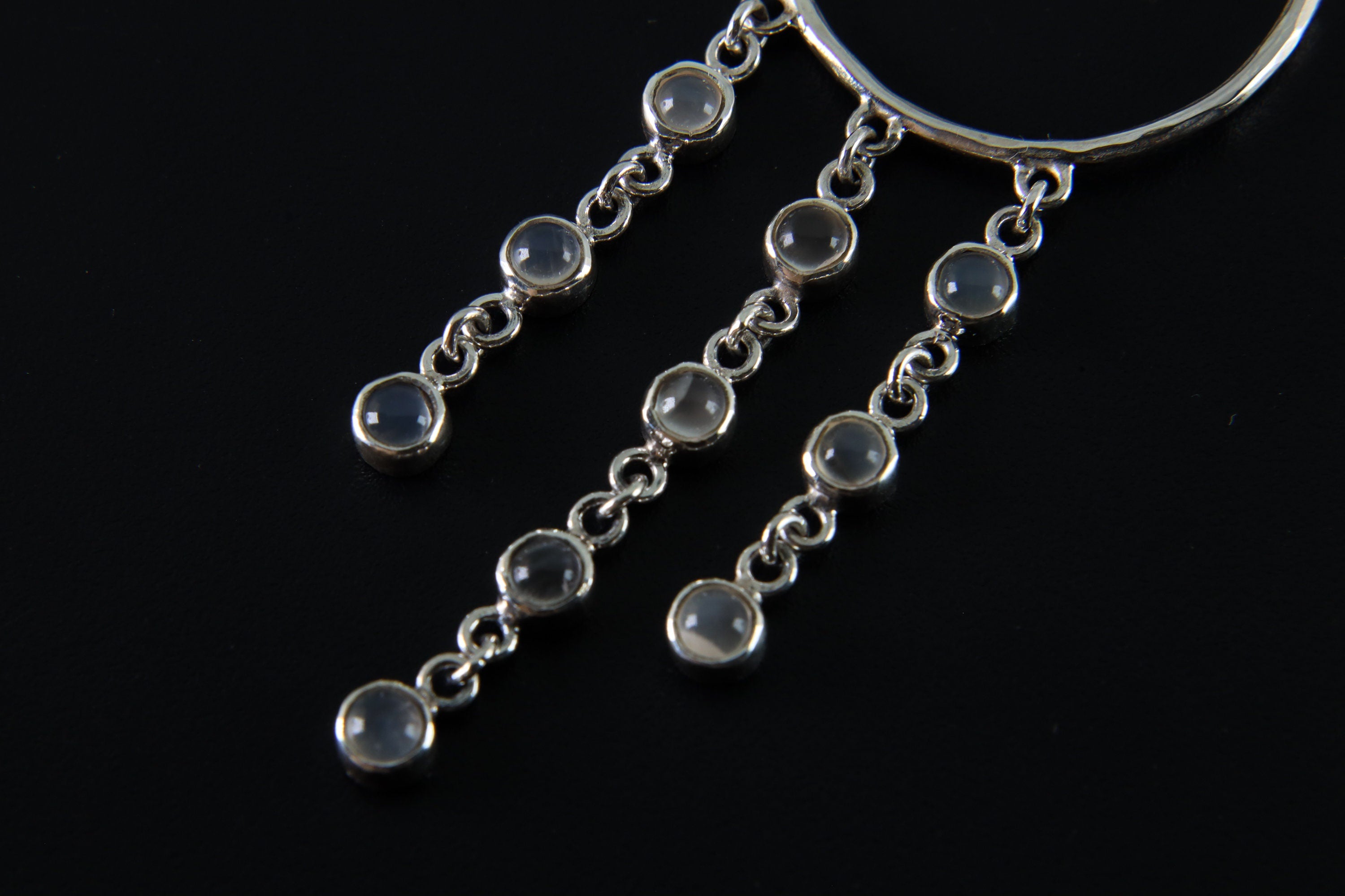 Close-up of Cat Eye Moonstone cascading hoop earring showing polished silver links and luminous round gemstones.