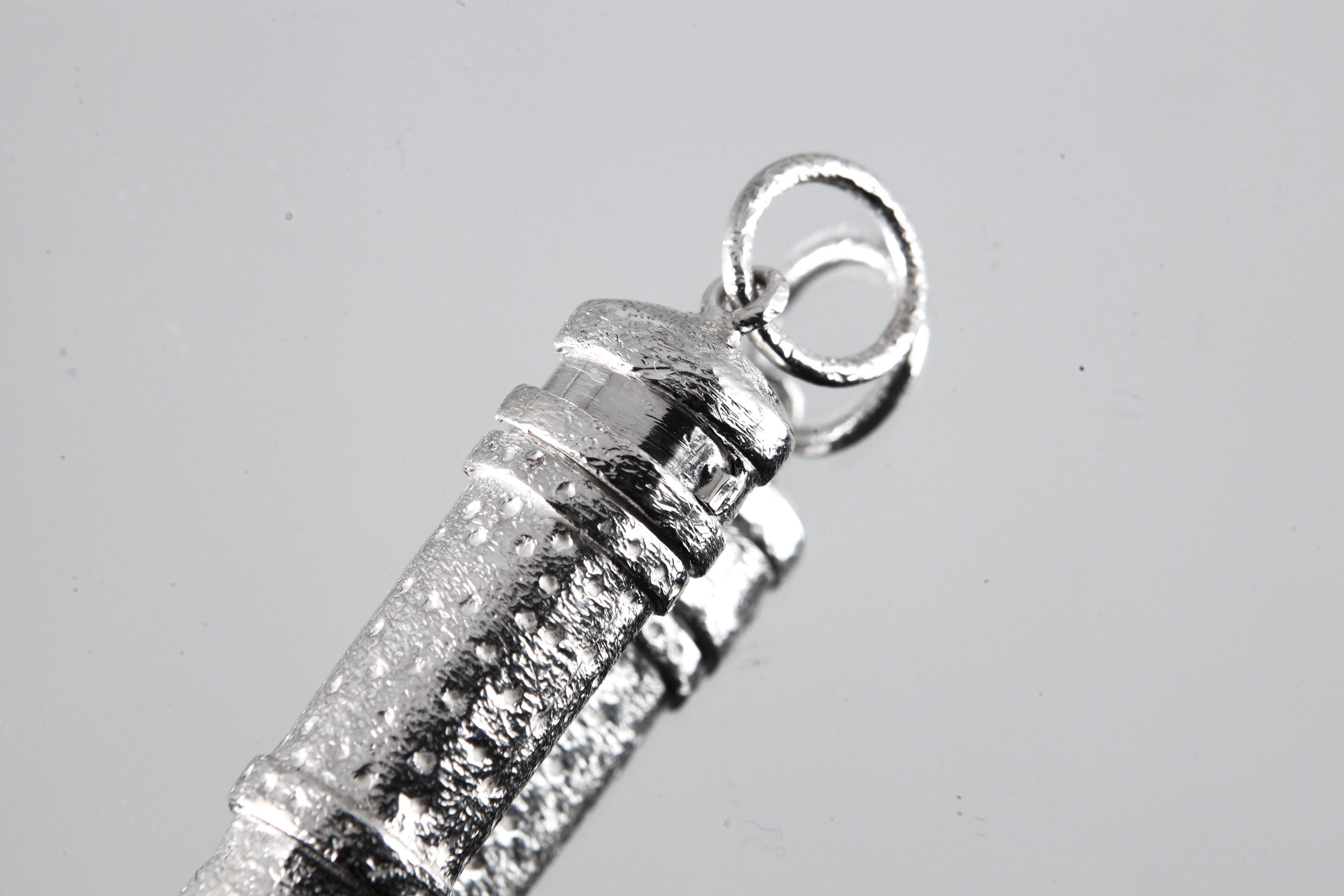 High-shine sterling silver capsule pendant showing round bail and textured detail.