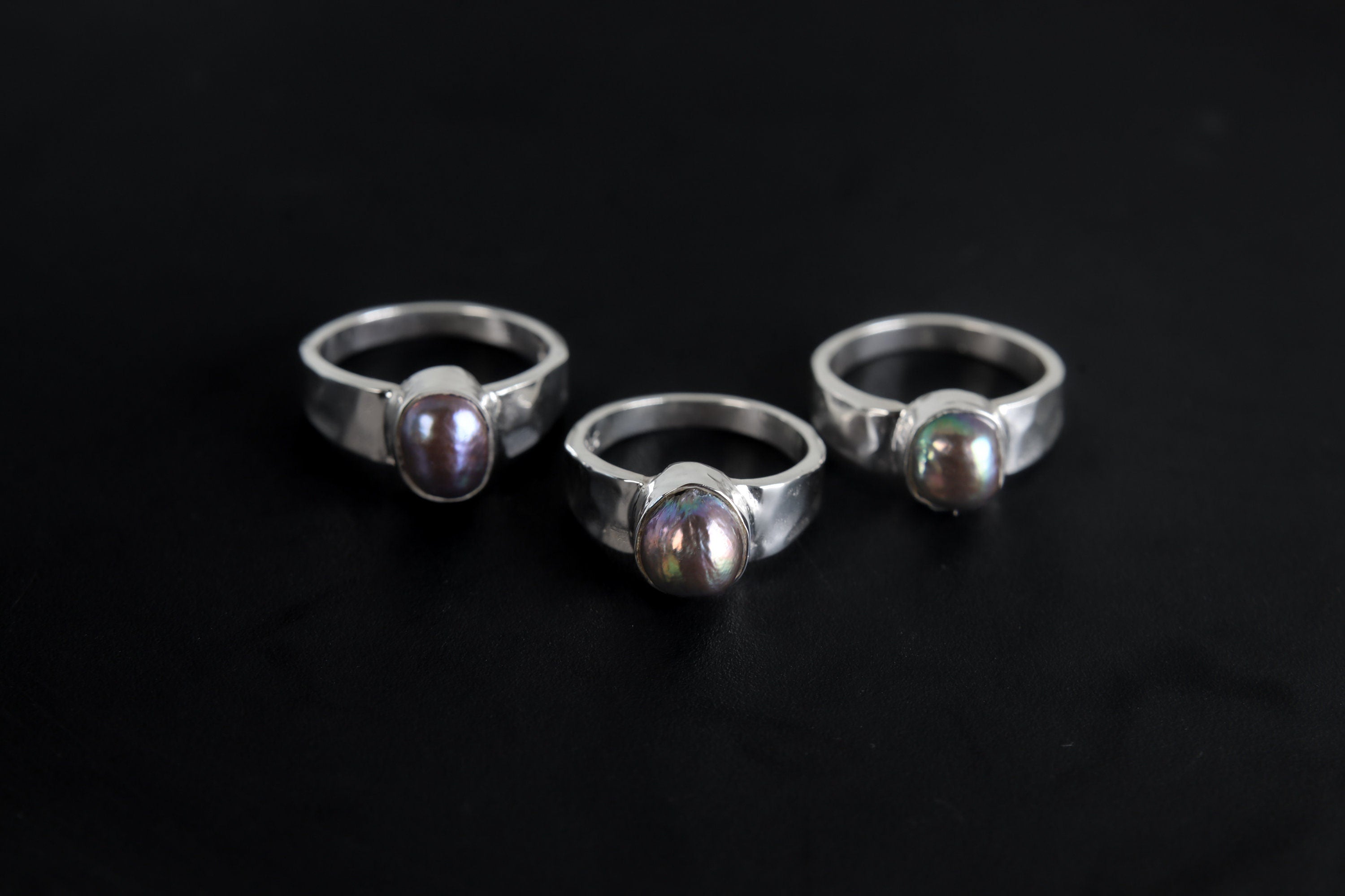 Group of Midnight Luster Black Pearl Rings shown on black background with hammered sterling silver bands and dark Pearls.
