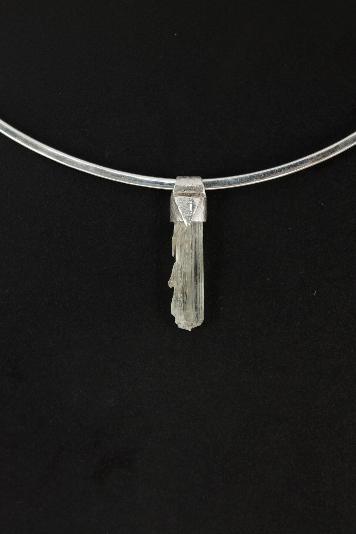 Skeletal Aquamarine Stack Pendant shown on black background with sterling silver cap and raw green-blue crystal body.
