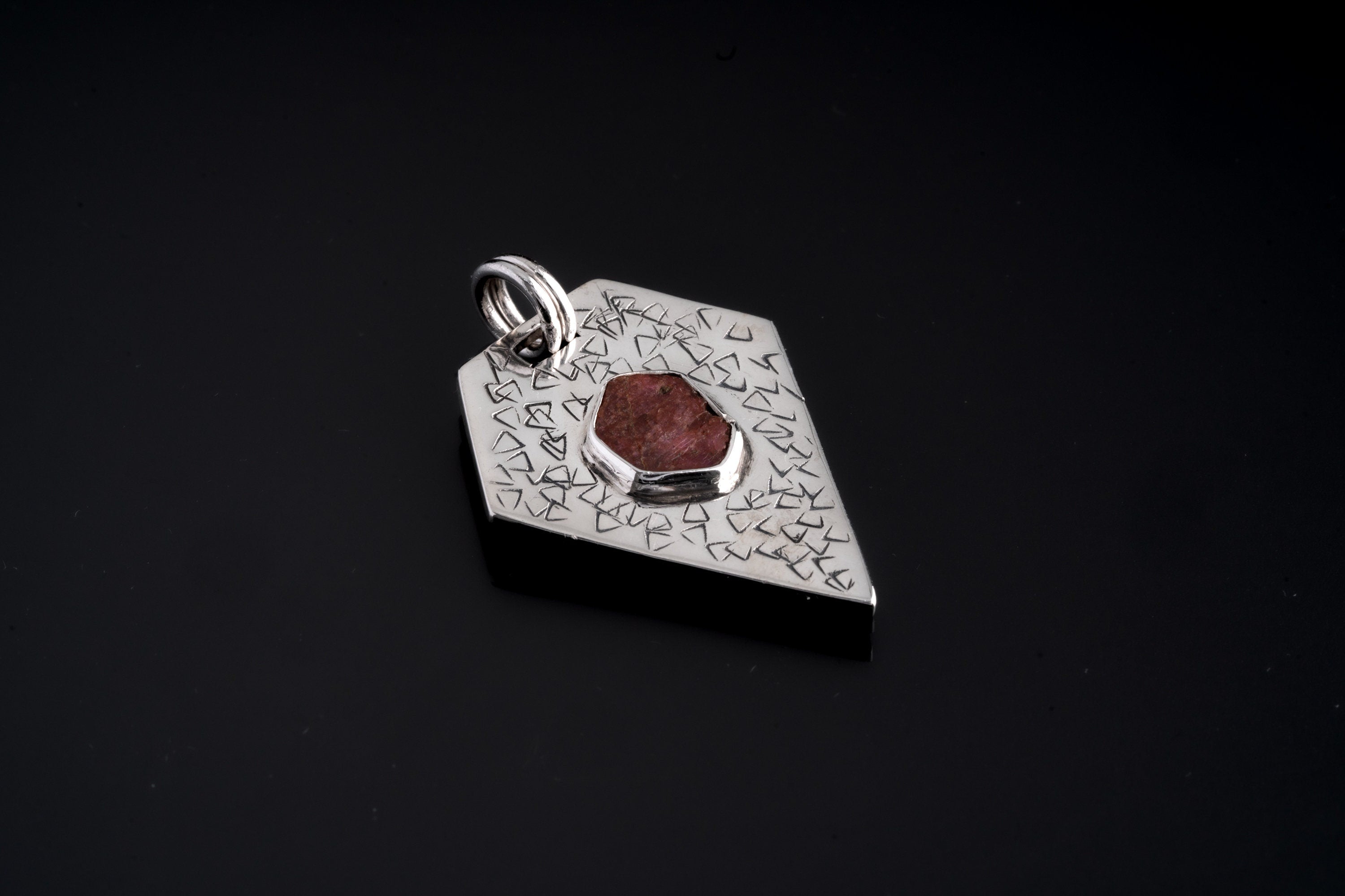 Record Keeper Ruby pendant on black background with oxidized sterling silver pentagon frame and abstract hand-textured surface.