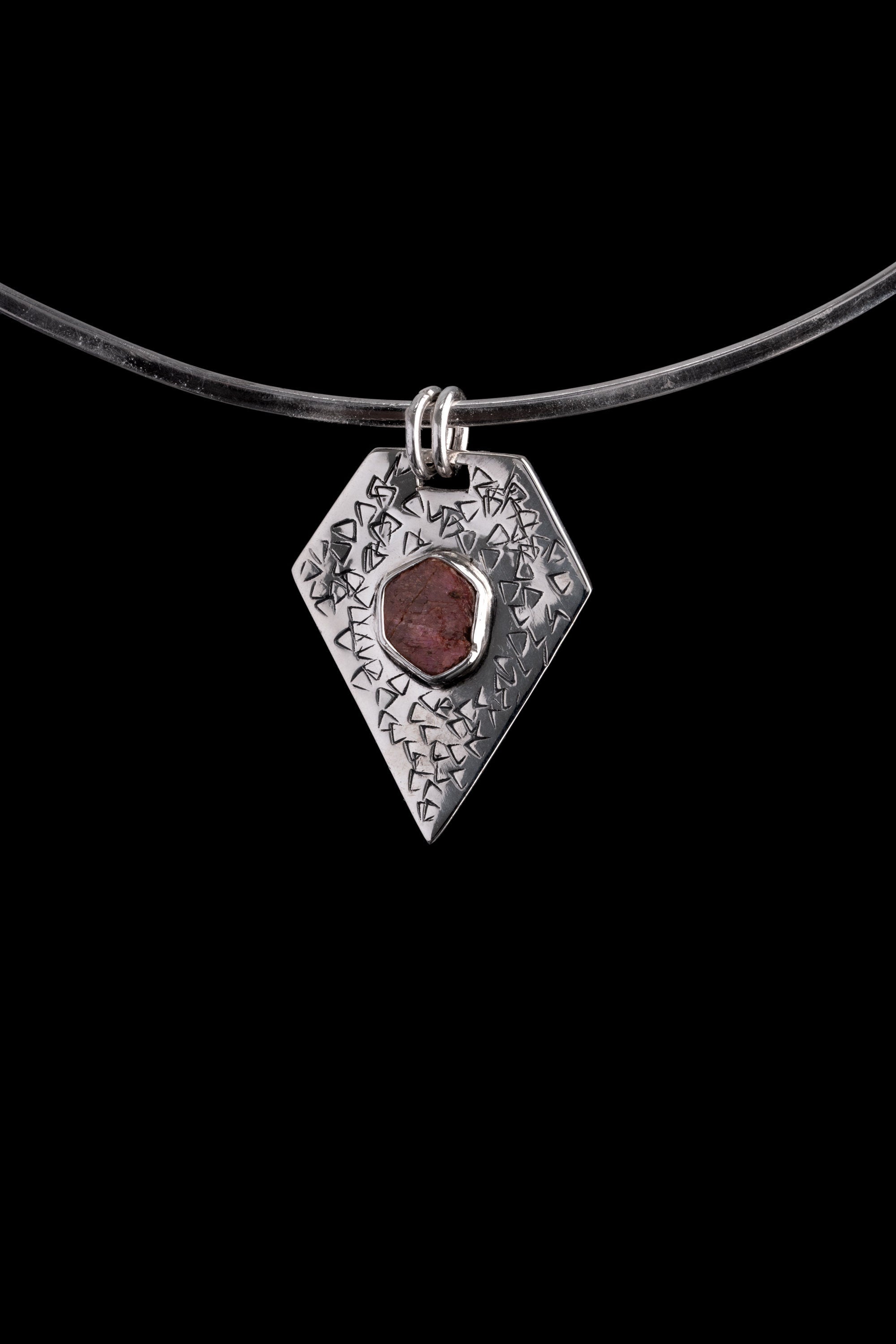 Geometric Ruby pentagon pendant shown on black cord, with twin circular bails and central bezel-set red stone.