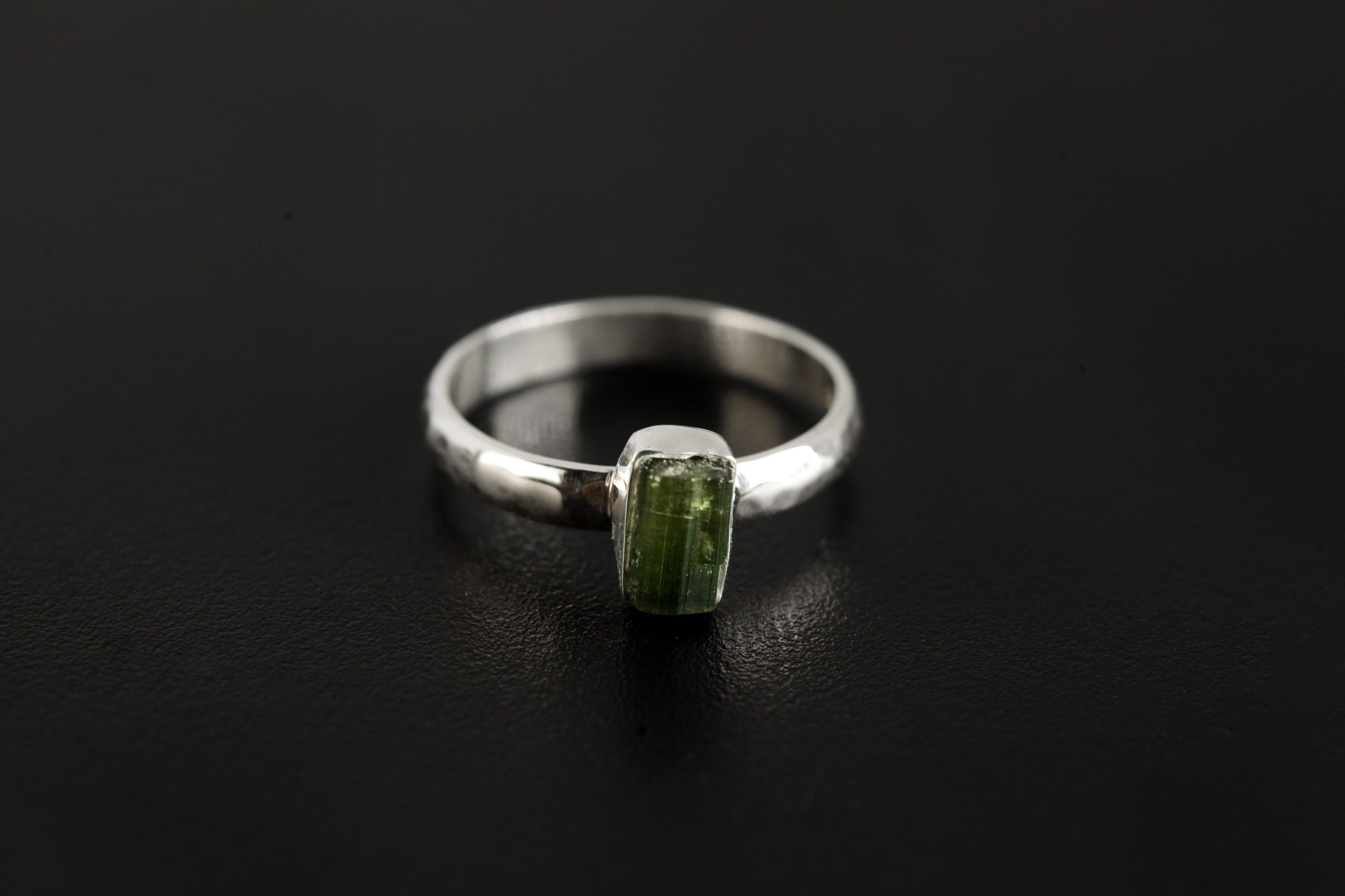 Green Tourmaline hammered silver ring shown on a dark background, with vertical green gemstone and polished 925 sterling silver band.