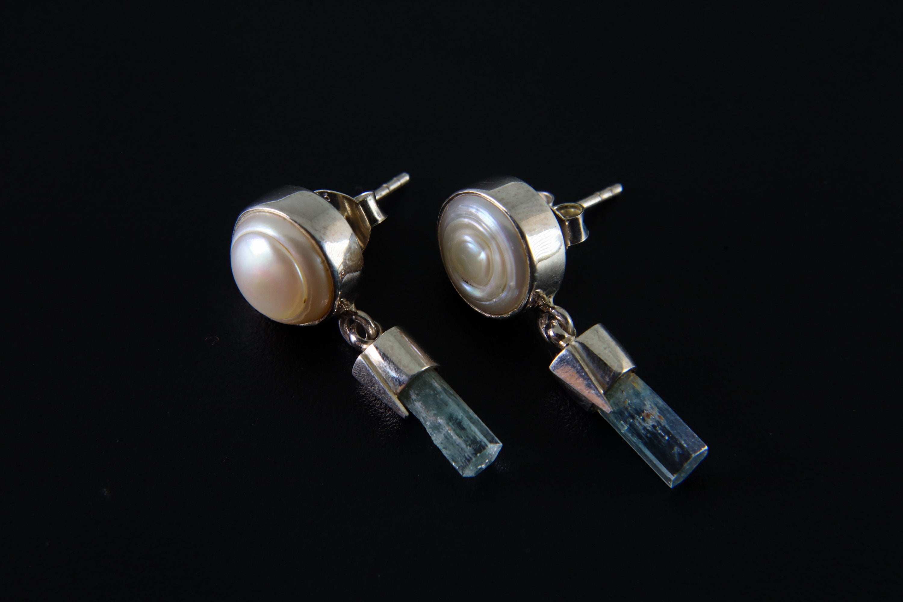South Sea Pearl and raw Aquamarine earrings shown on dark background, with sterling silver stud fittings and crystal dangles.