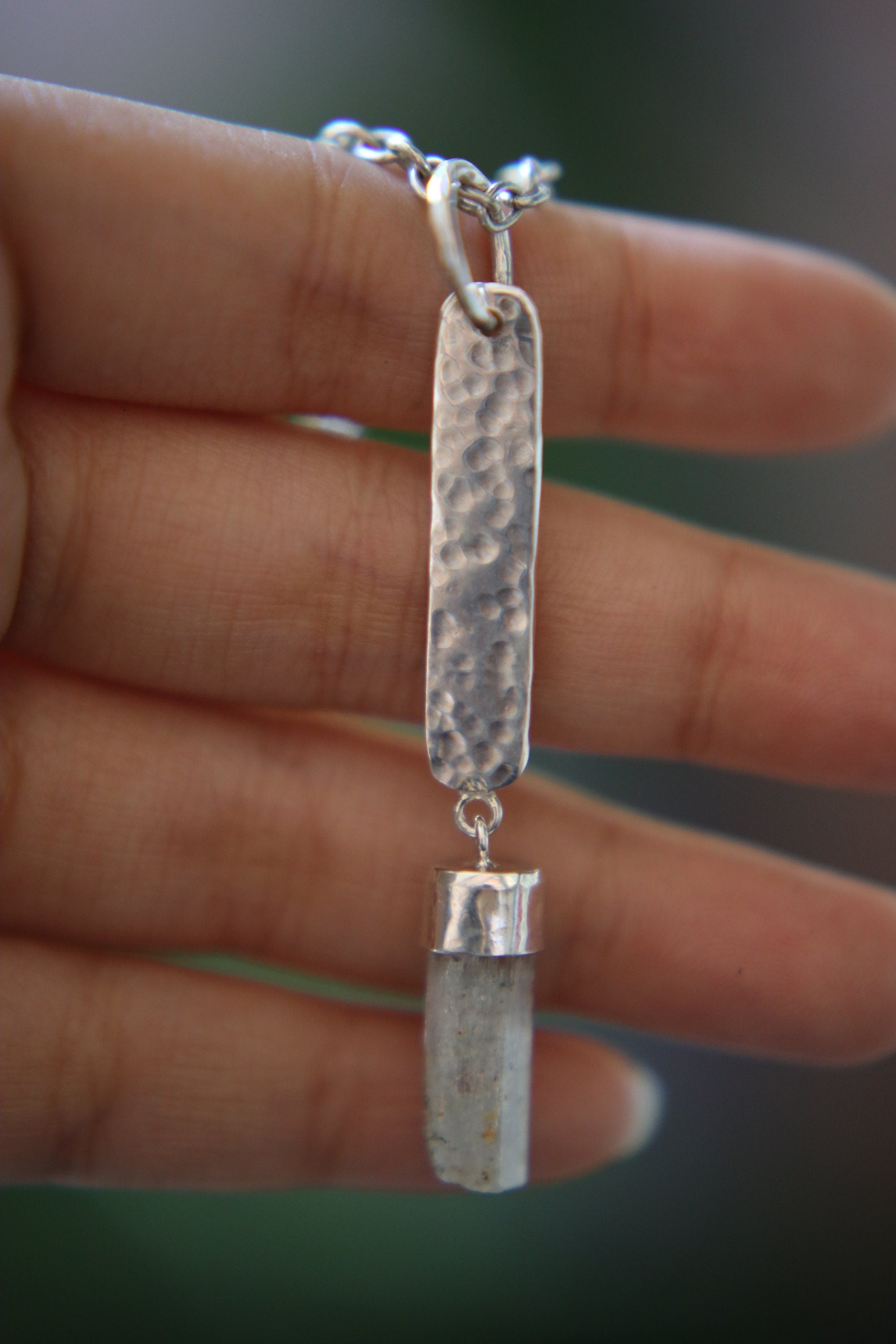 Aquamarine sterling silver pendant held in hand, showing raw crystal detail and textured rectangular silver plate.
