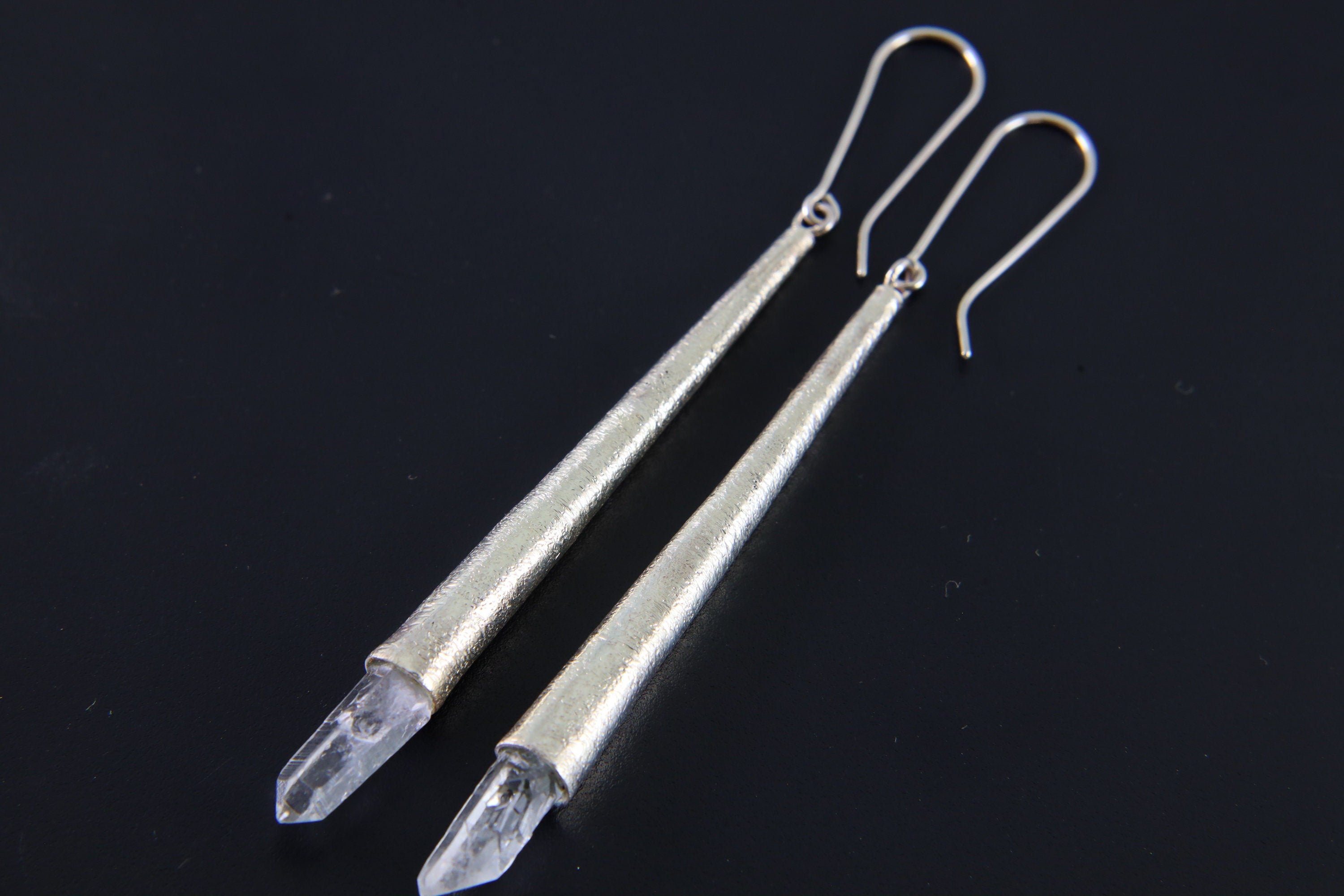 Long sterling silver cone earrings shown on dark background with raw Diamond Quartz crystal points.