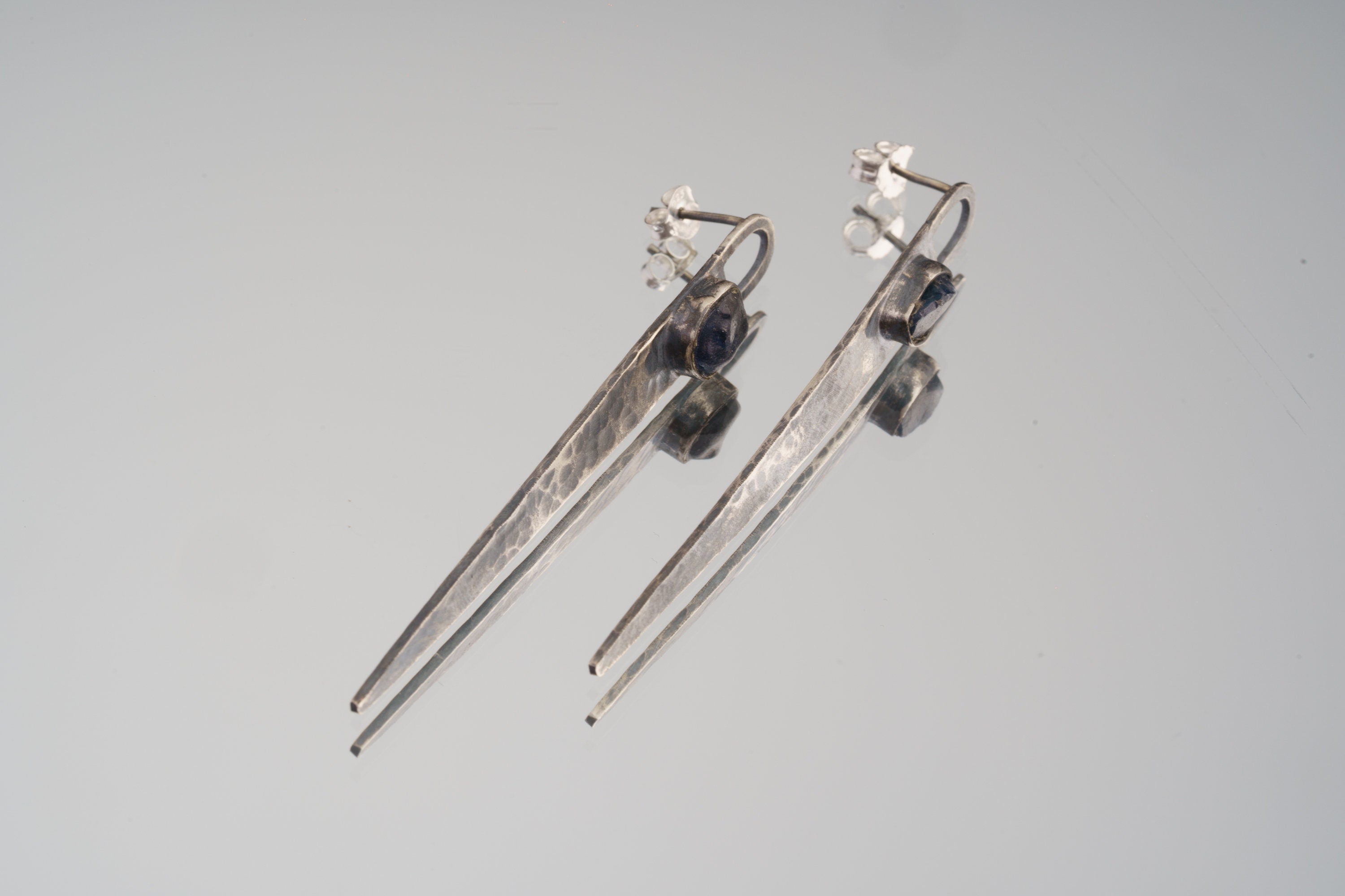 Sapphire hammered sterling silver earrings displayed on light background with long tapered oxidized silver forms.