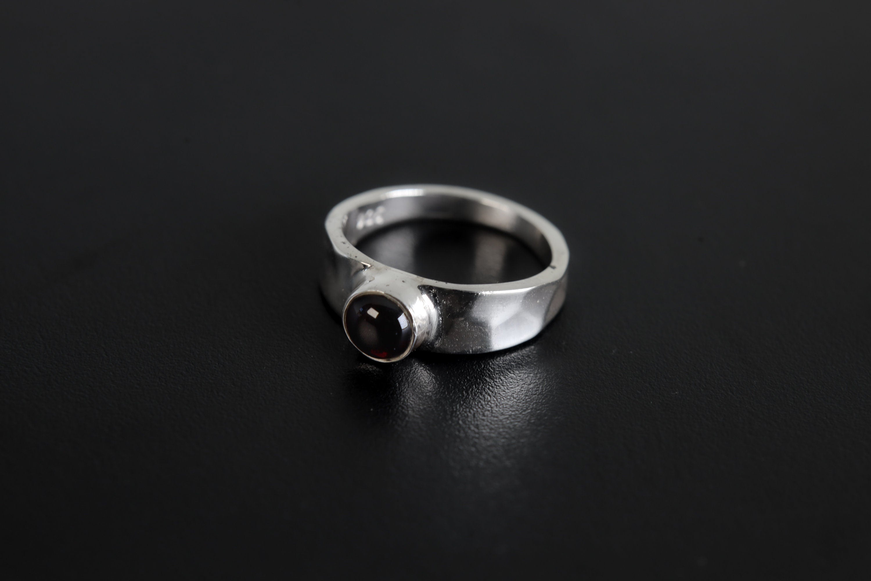 Crimson Sentinel Garnet Ring shown on black background with deep crimson stone and high-shine silver band.
