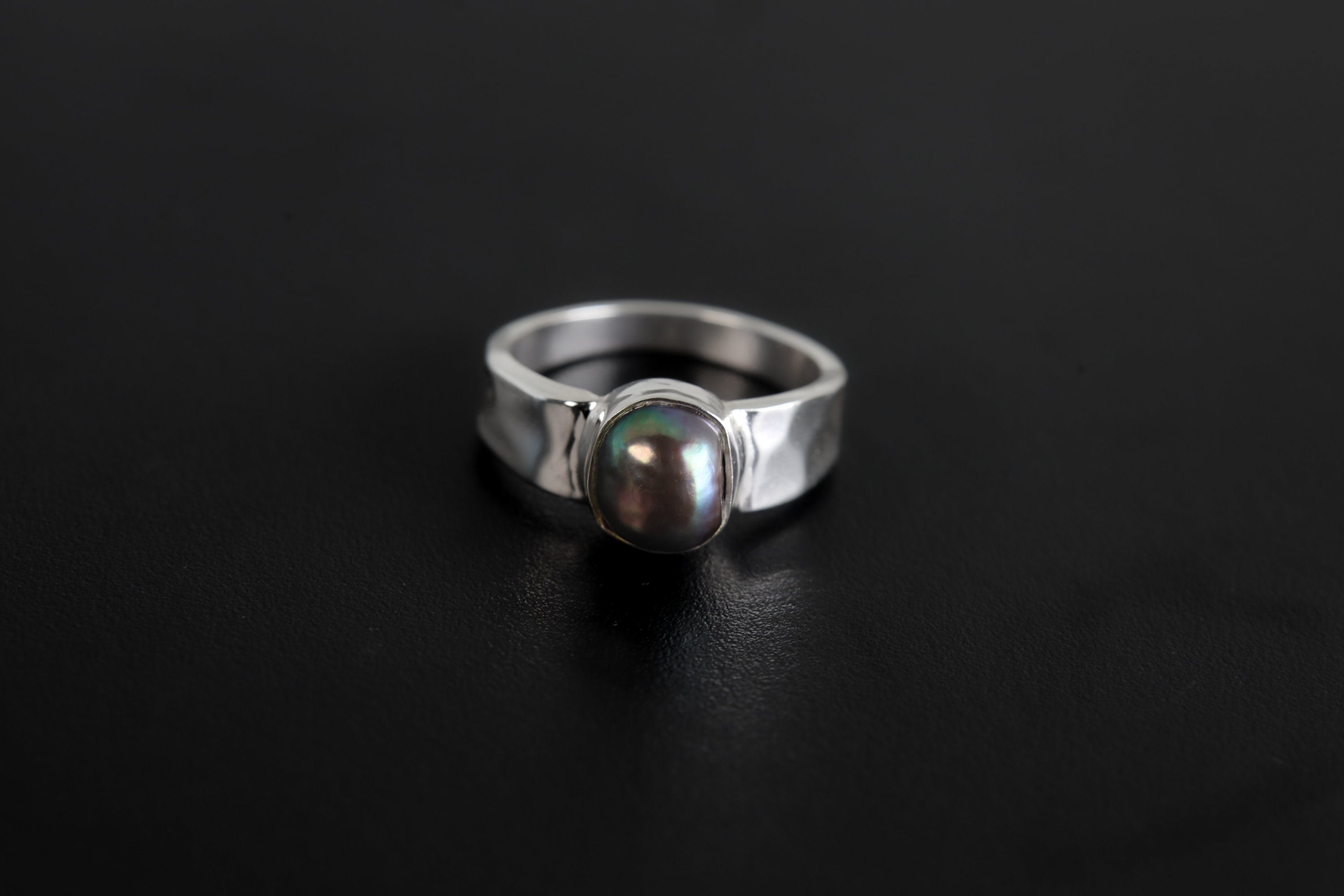 Midnight Luster Black Pearl Ring shown on black background with hammered silver band and smooth dark Pearl centre.