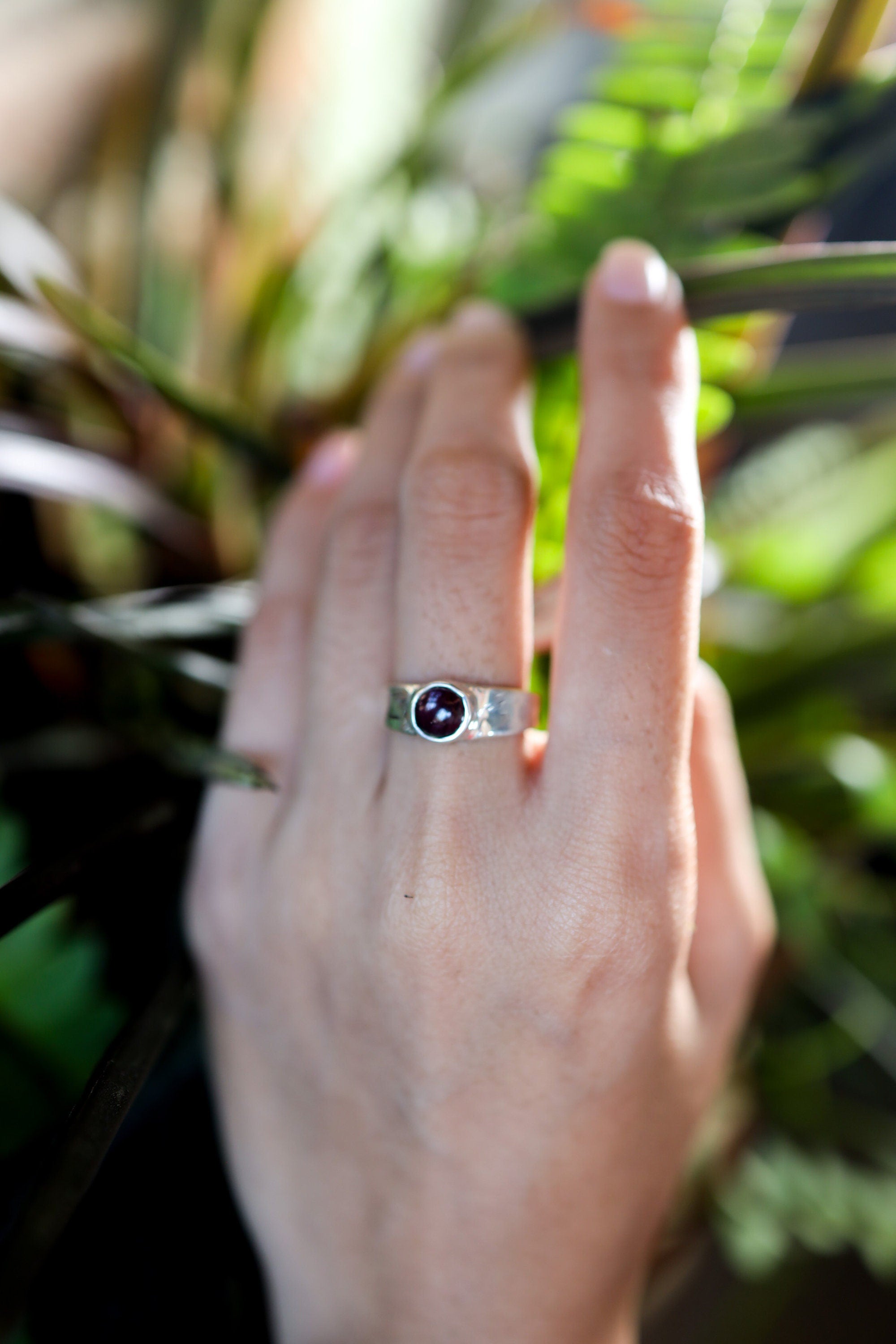 Crimson Sentinel Garnet Ring shown worn outdoors with deep red stone and hammered 925 silver texture.