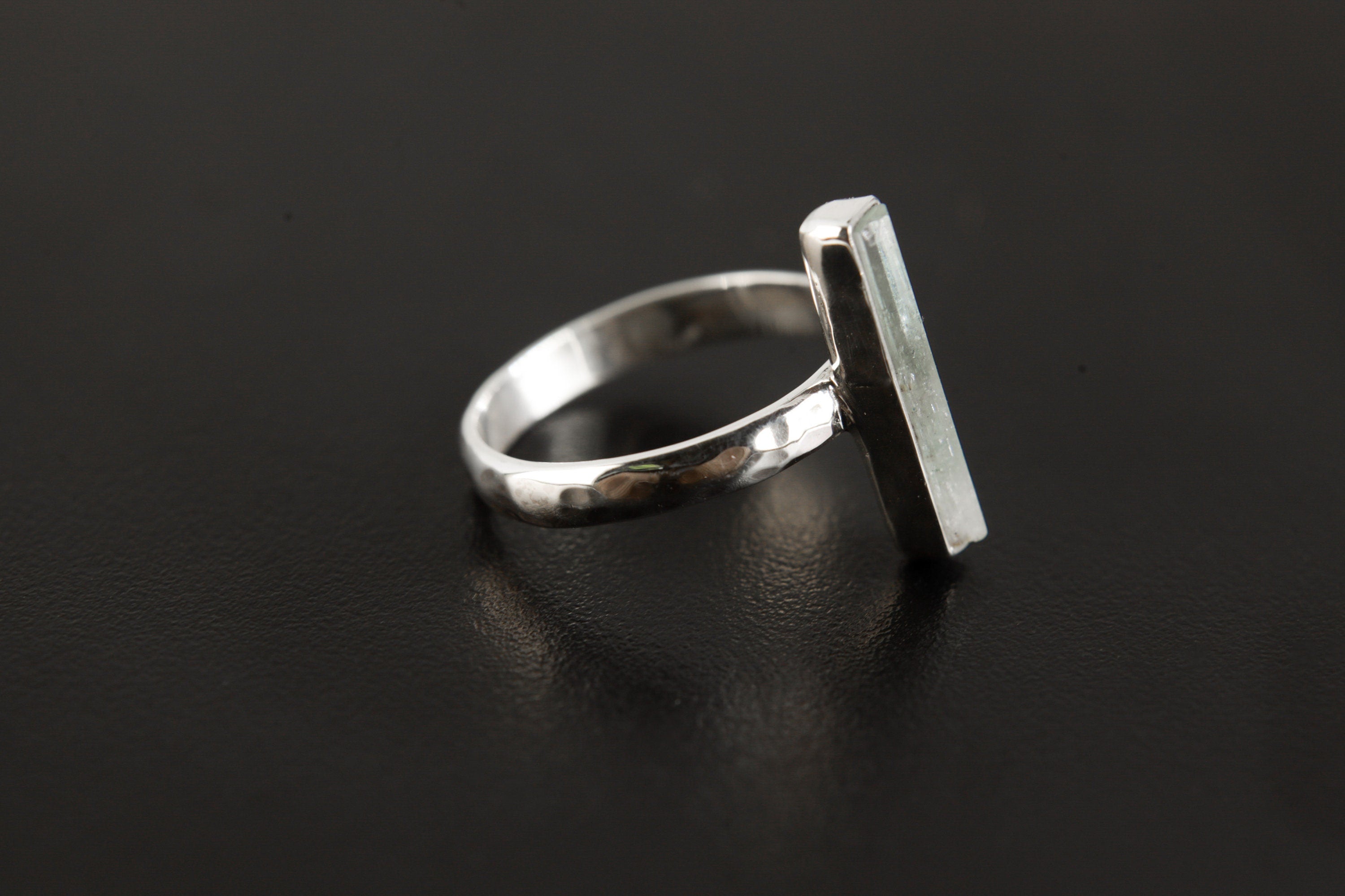 Side view of long square cut Aquamarine ring showing hammered sterling silver band and slim vertical gemstone setting.