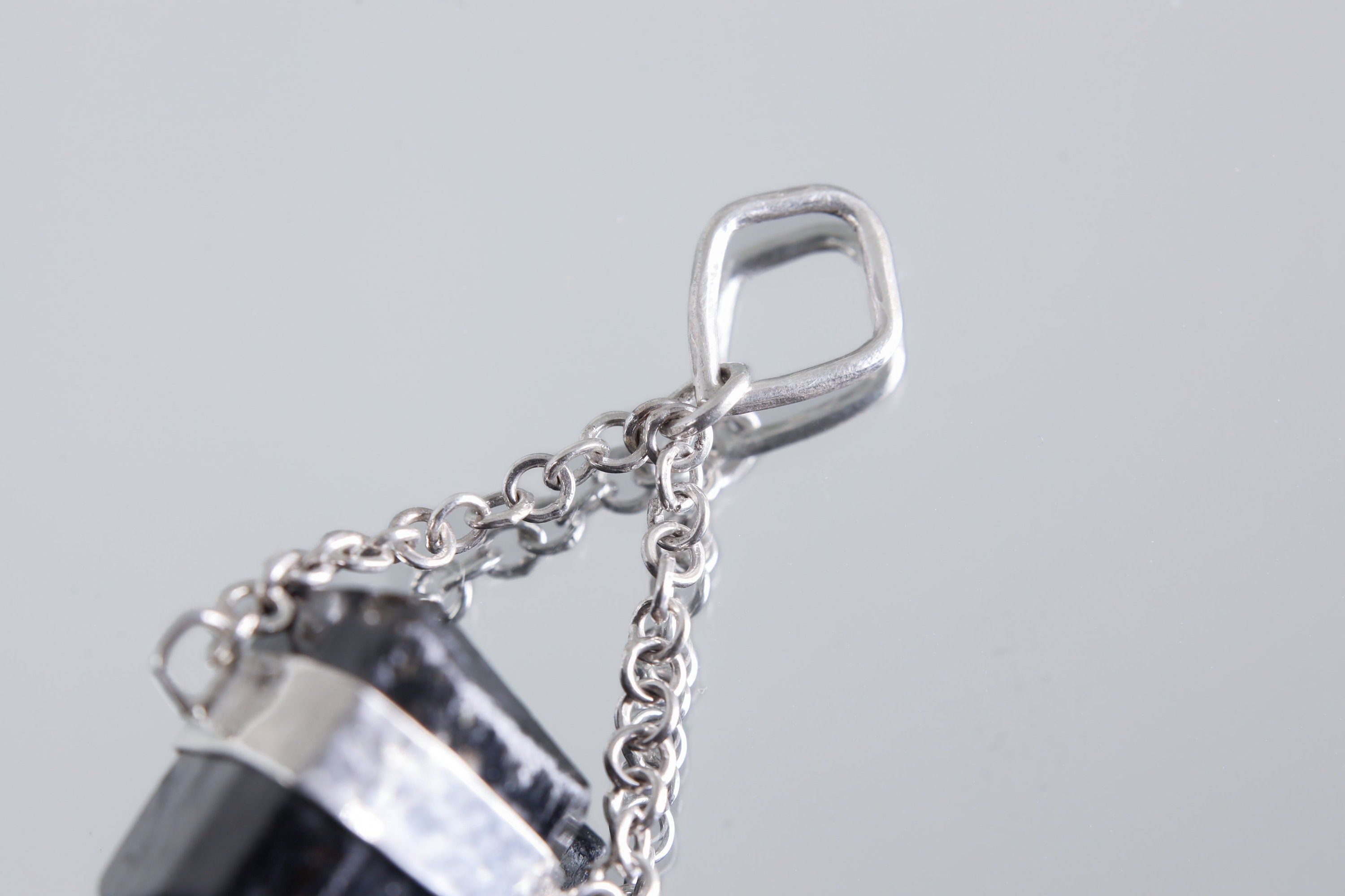 Black Tourmaline protection pendant shown with chain on white background and handmade silver detail.