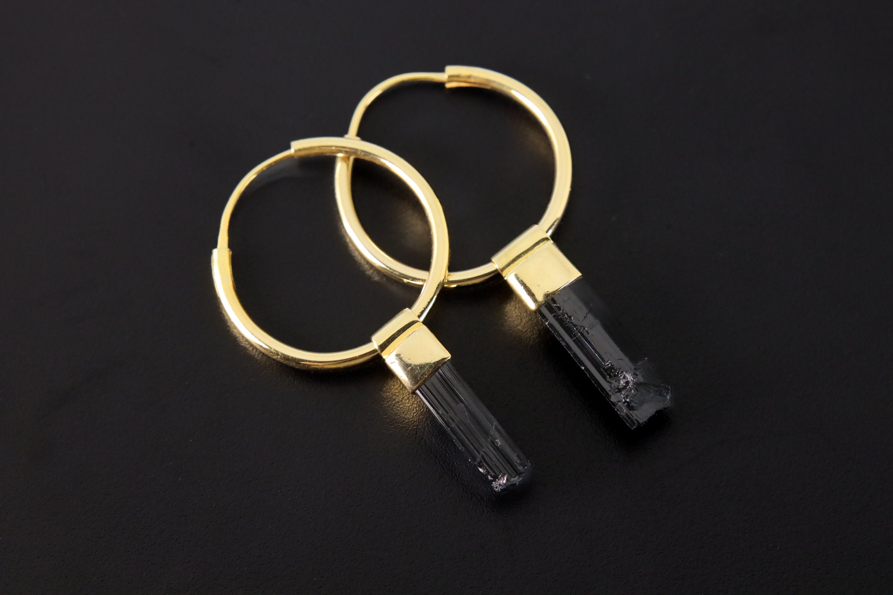 Black Tourmaline convertible earrings shown on a dark background with gold-plated hoops and raw black wand crystals.