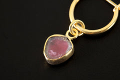 Close-up of Watermelon Tourmaline hoop earring pendant showing prong-set gem slice and polished gold finish.