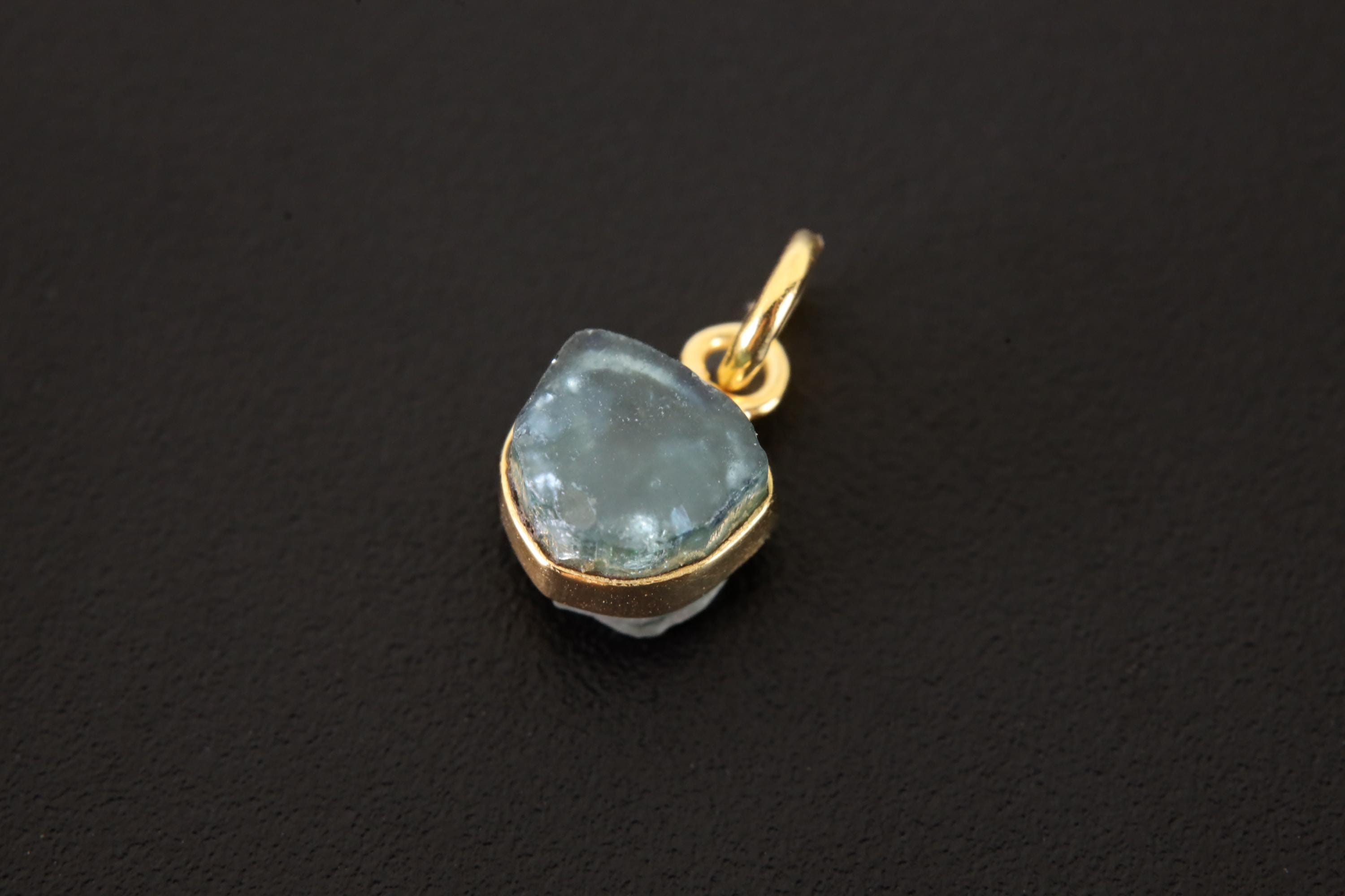 Raw Blue Tourmaline slice pendant charm shown on dark background with gold-plated sterling silver setting.
