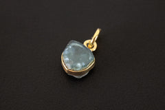 Raw Blue Tourmaline slice pendant charm shown on dark background with gold-plated sterling silver setting.