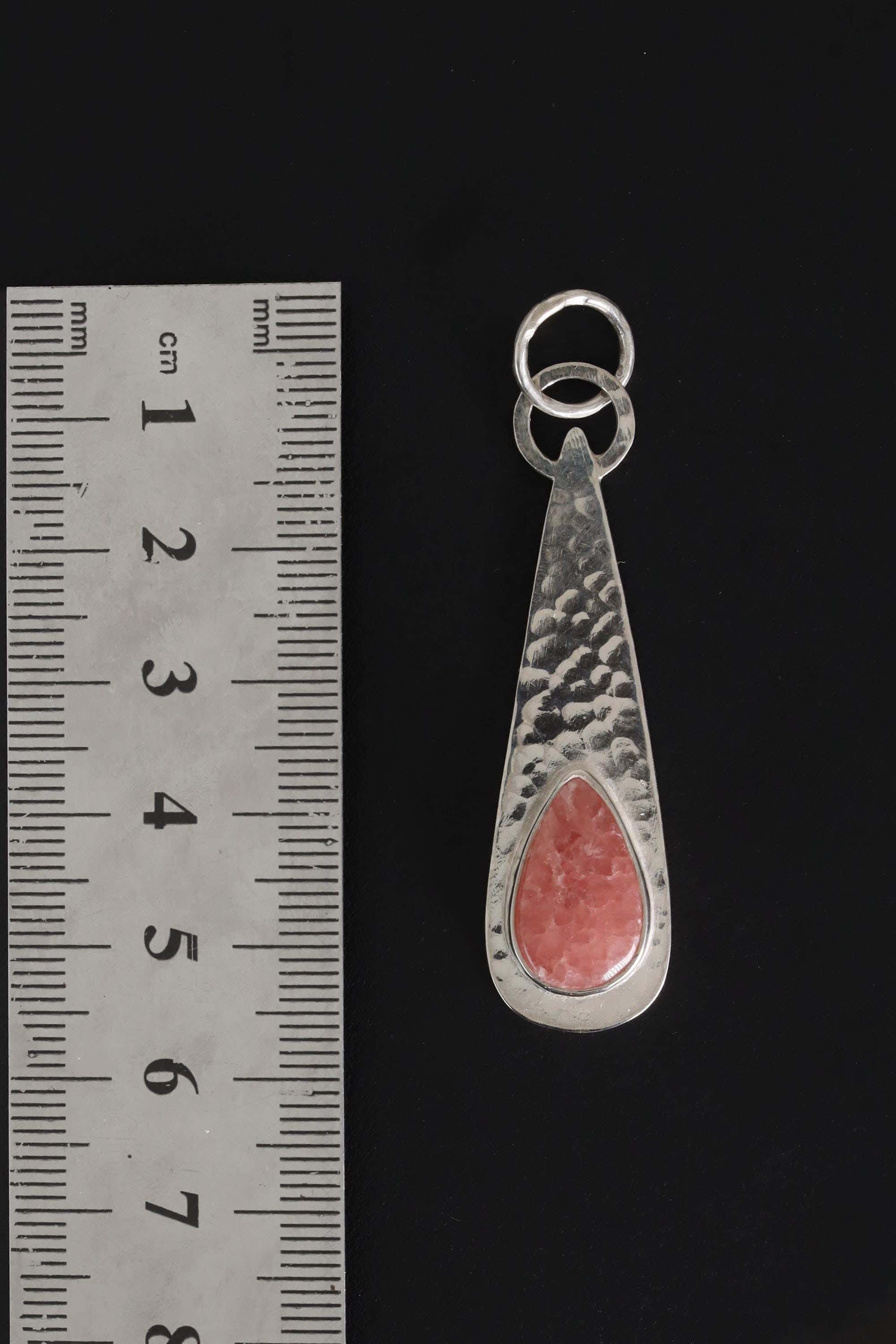 Rhodochrosite sterling silver teardrop pendant shown beside a ruler for scale with round bail and hammered texture.