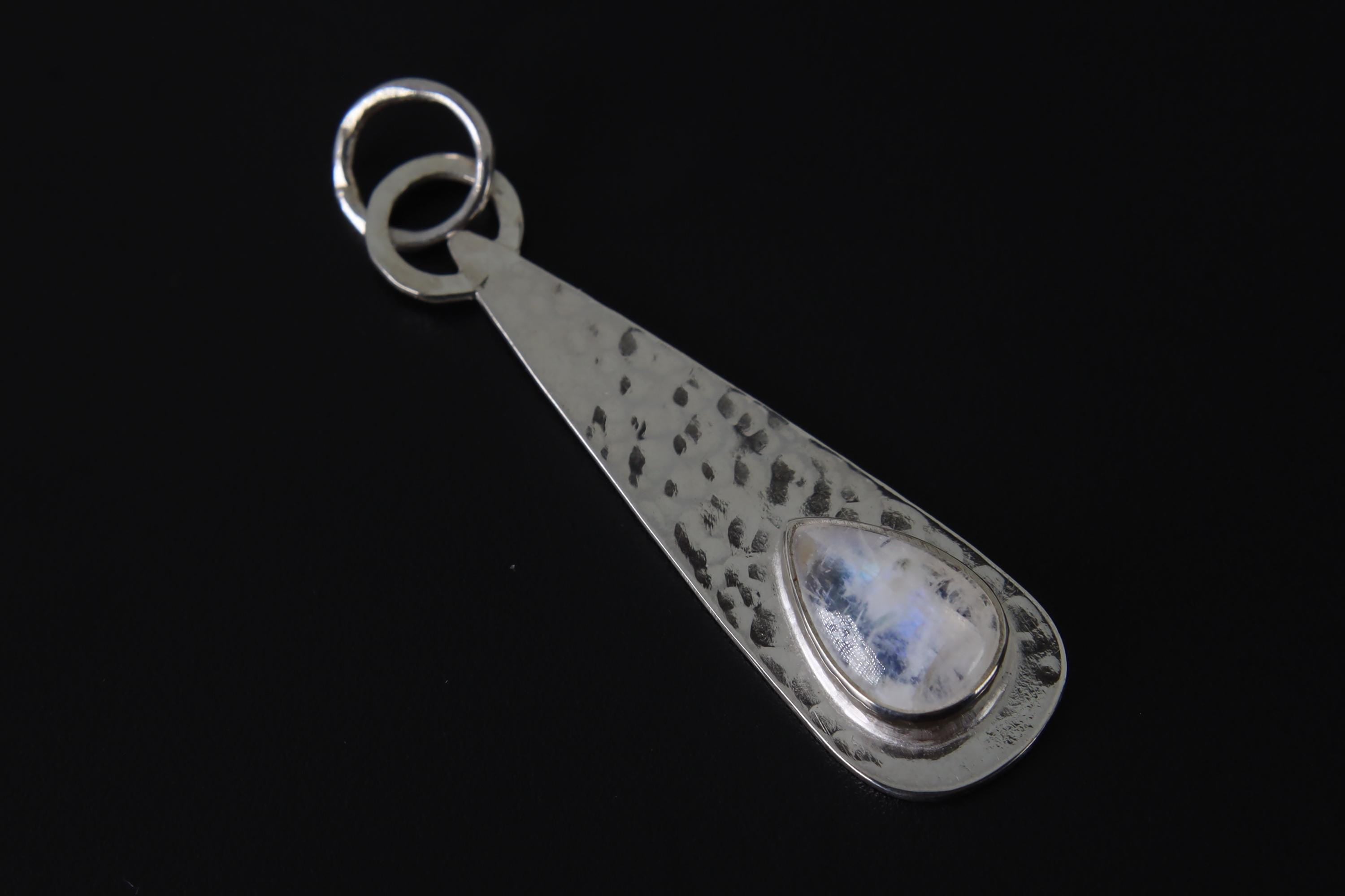 Lunar Teardrop Blue Moonstone pendant shown on dark background with shiny hammered sterling silver and blue flash stone.