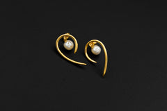 Gold-plated Pearl stud earrings shown on a dark background, with sculptural curled horn design and soft Pearl glow.