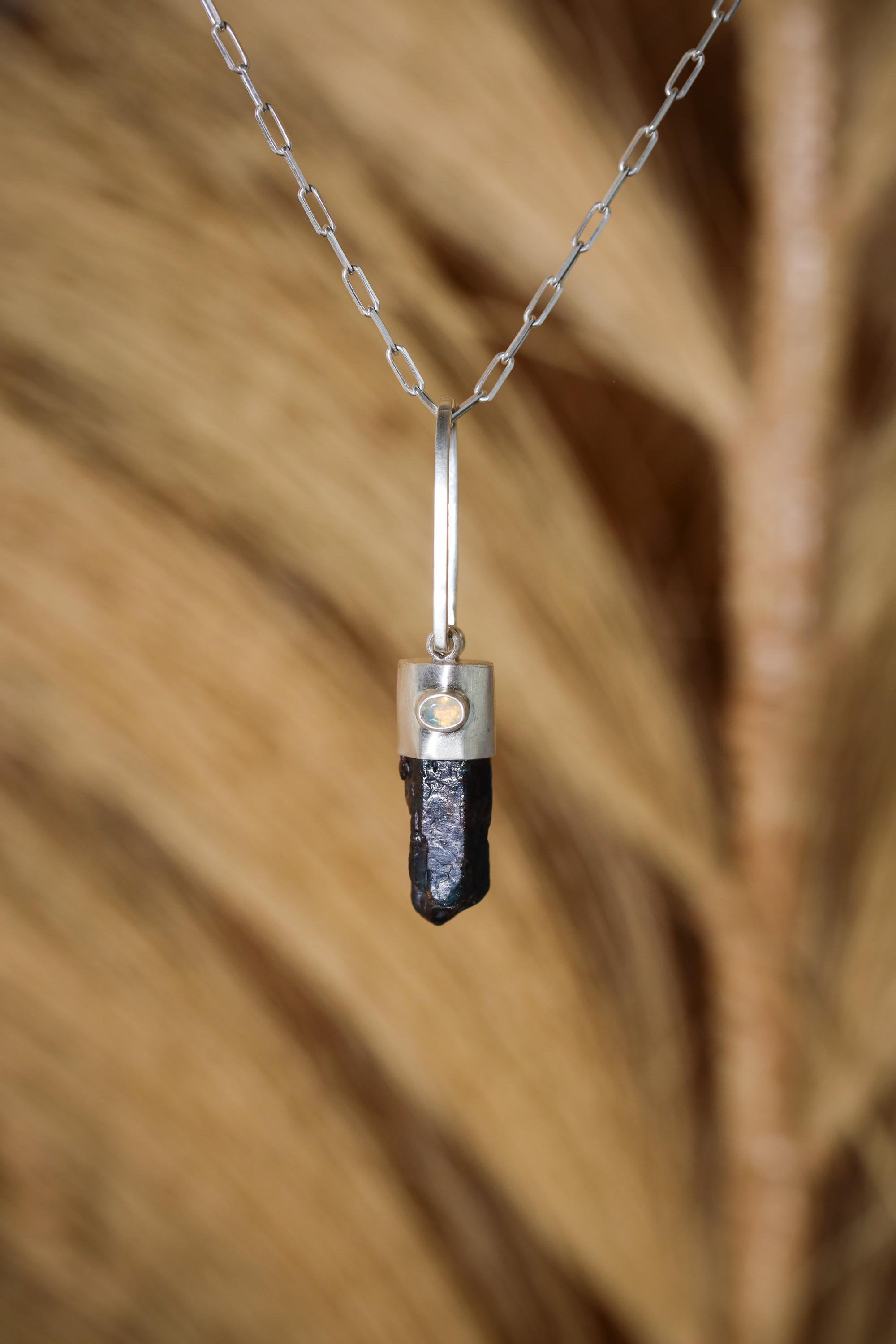 Blue Apatite Ethiopian Opal pendant shown hanging against natural grass texture, with silver chain and vivid blue crystal point.