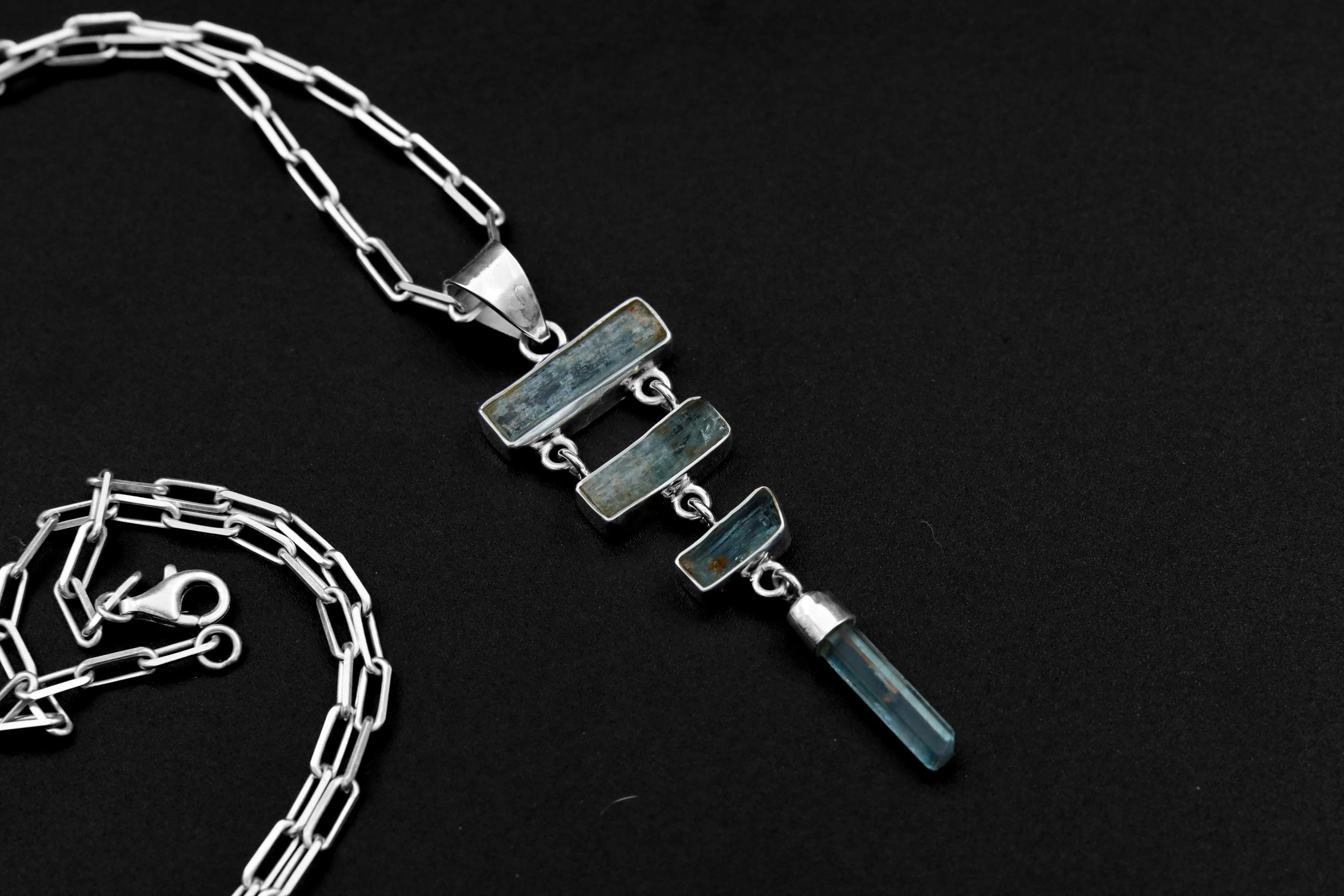 Raw Aquamarine cascade pendant in 925 sterling silver with four blue stones, open-back bezels, and a black necklace cord.