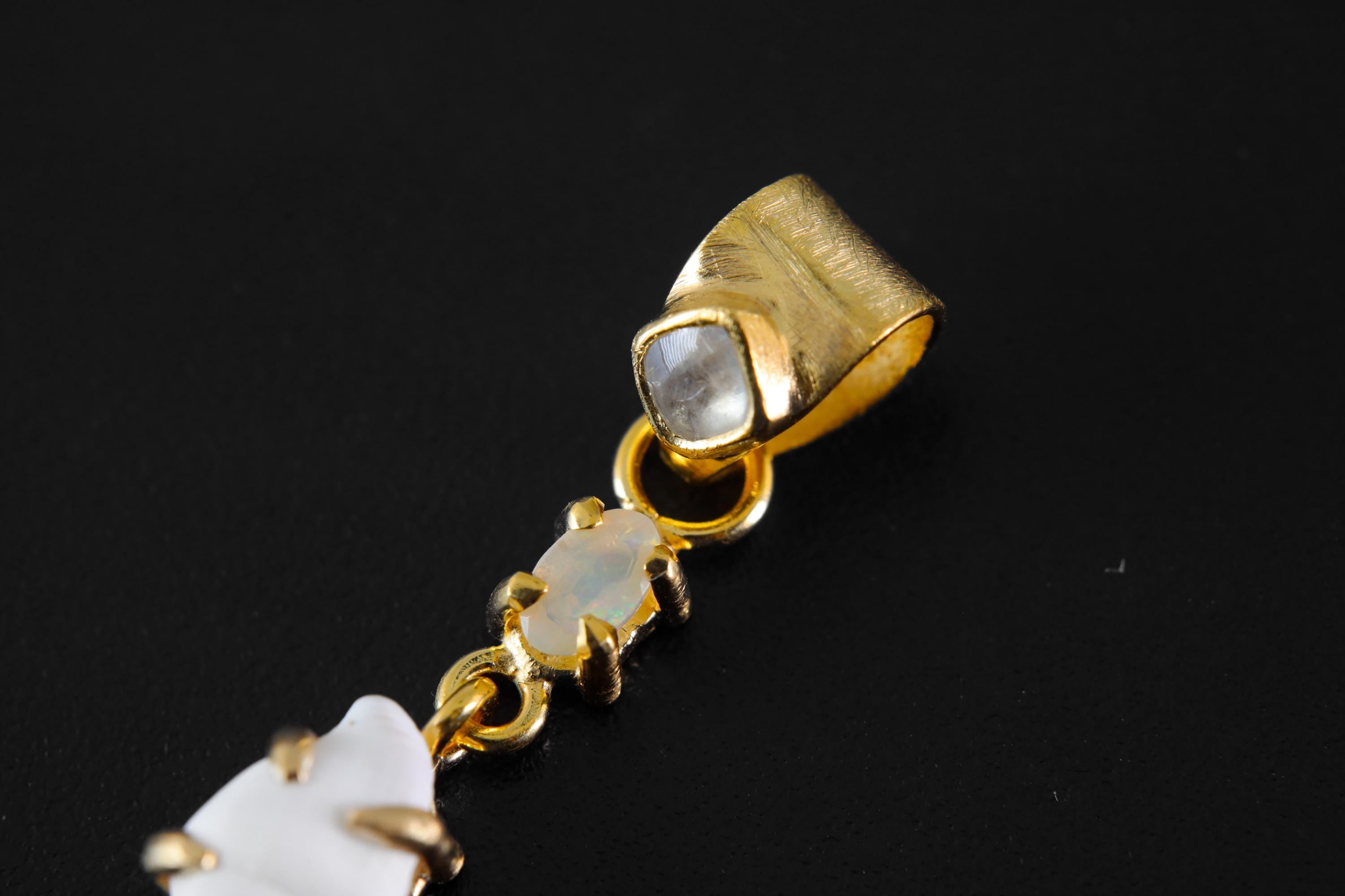 Detail view of semi-fossilized shell in a gold-plated claw setting, with Moonstone and Opal stones linked above.