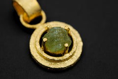 Close-up of raw Peridot pendant showing green crystal texture, sand-textured gold-plated setting, and wide bail.
