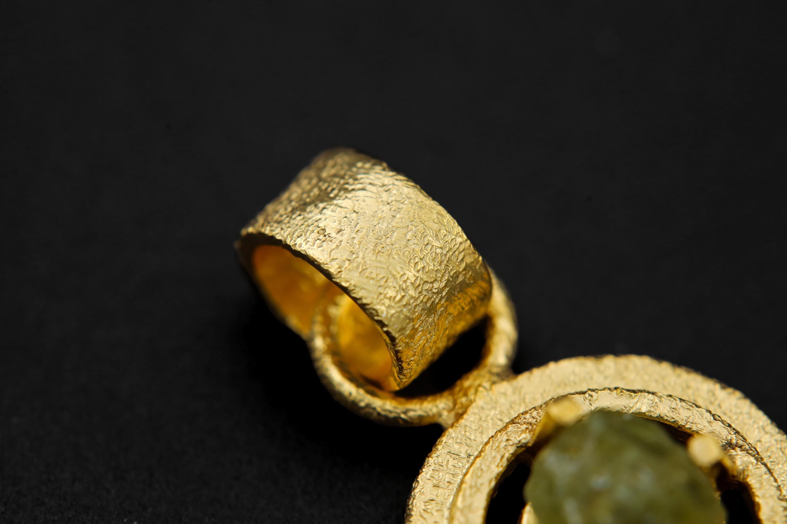 Close-up of raw Peridot pendant showing green crystal texture, sand-textured gold-plated setting, and wide bail.