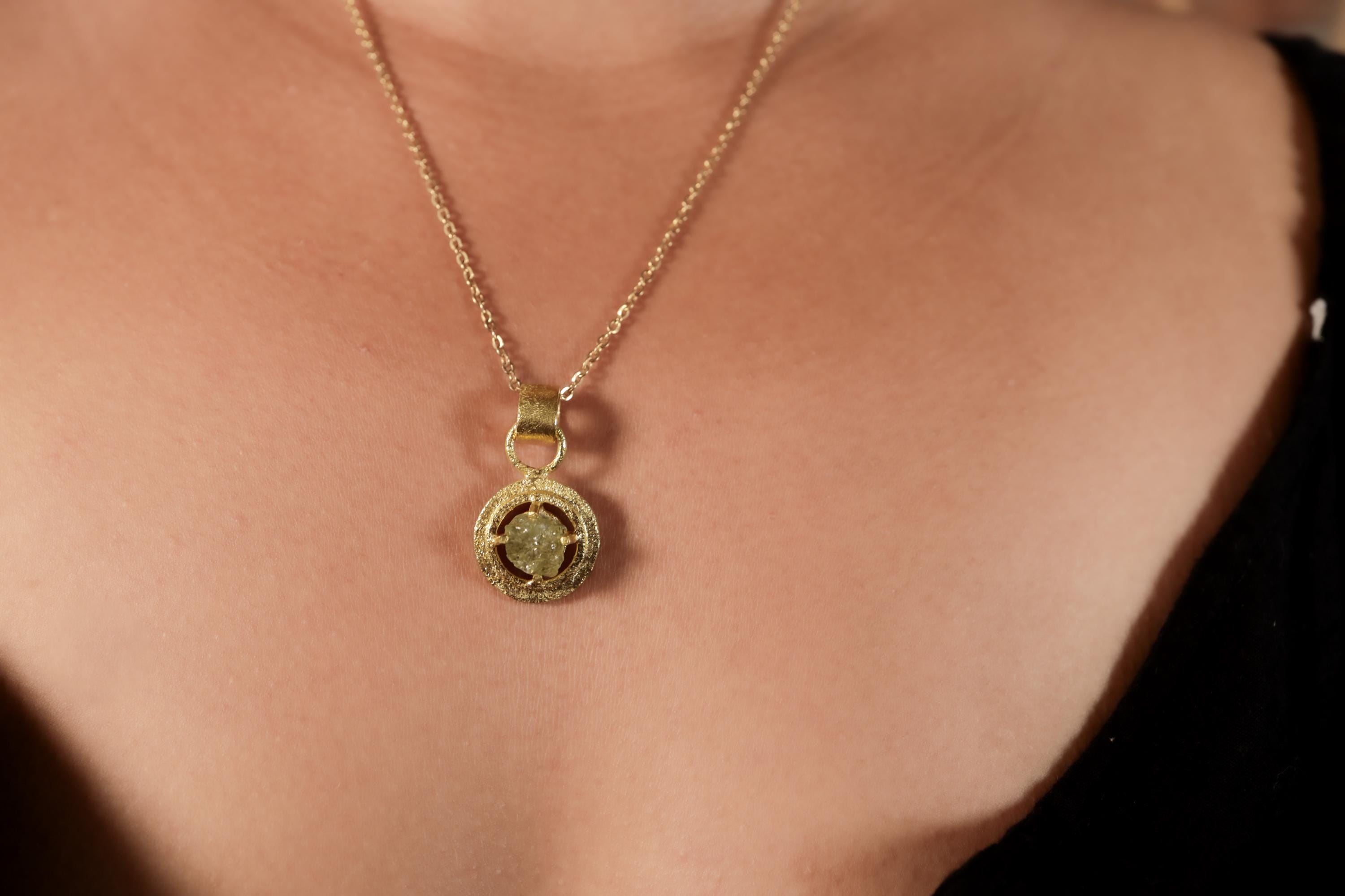 Raw AAA Peridot pendant shown worn on a necklace, with bright green stone and warm gold-plated talisman setting.