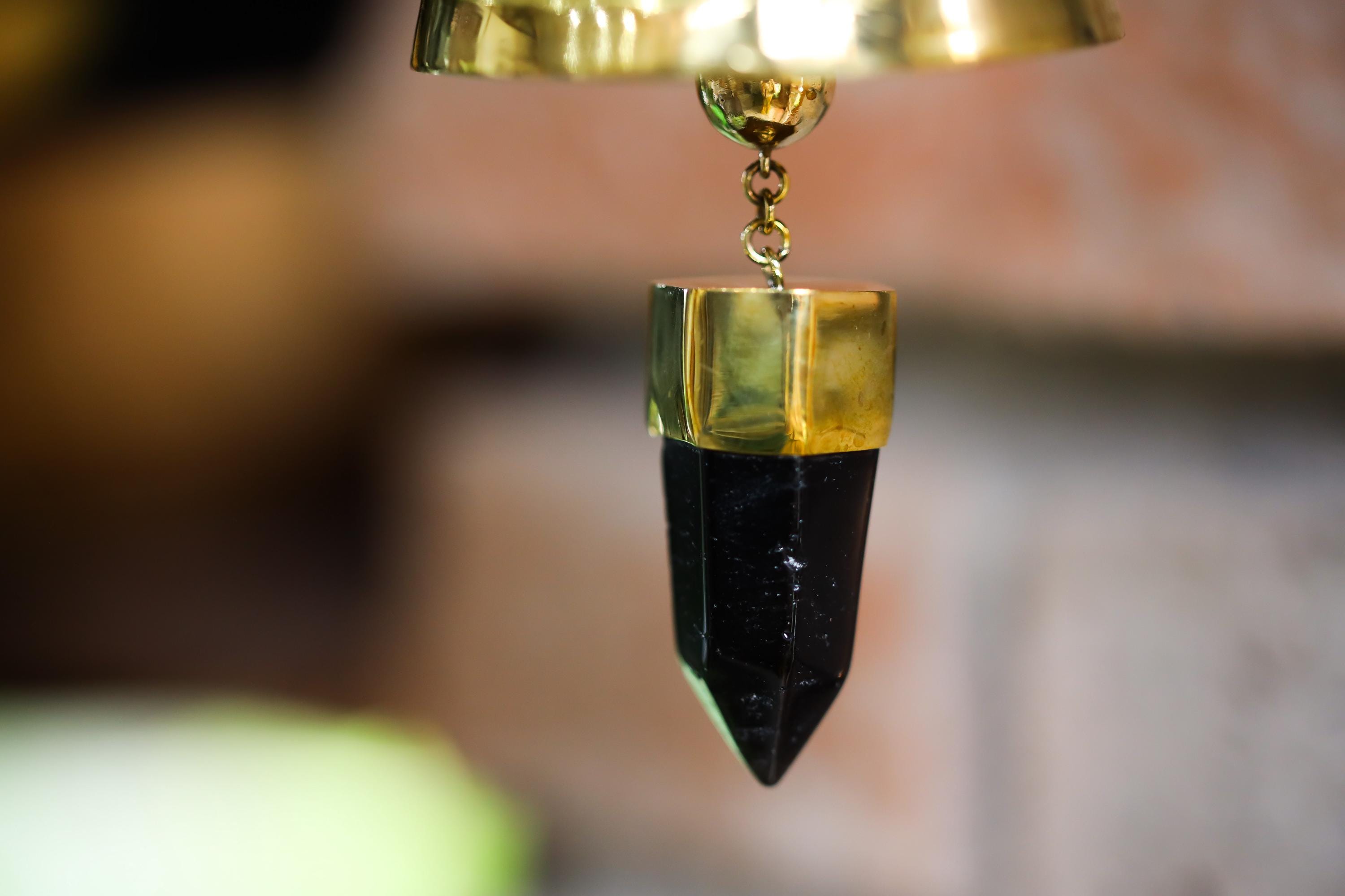 Close-up of Smoky Quartz point suspended inside gold-plated bronze prayer bell with dark crystal tip.