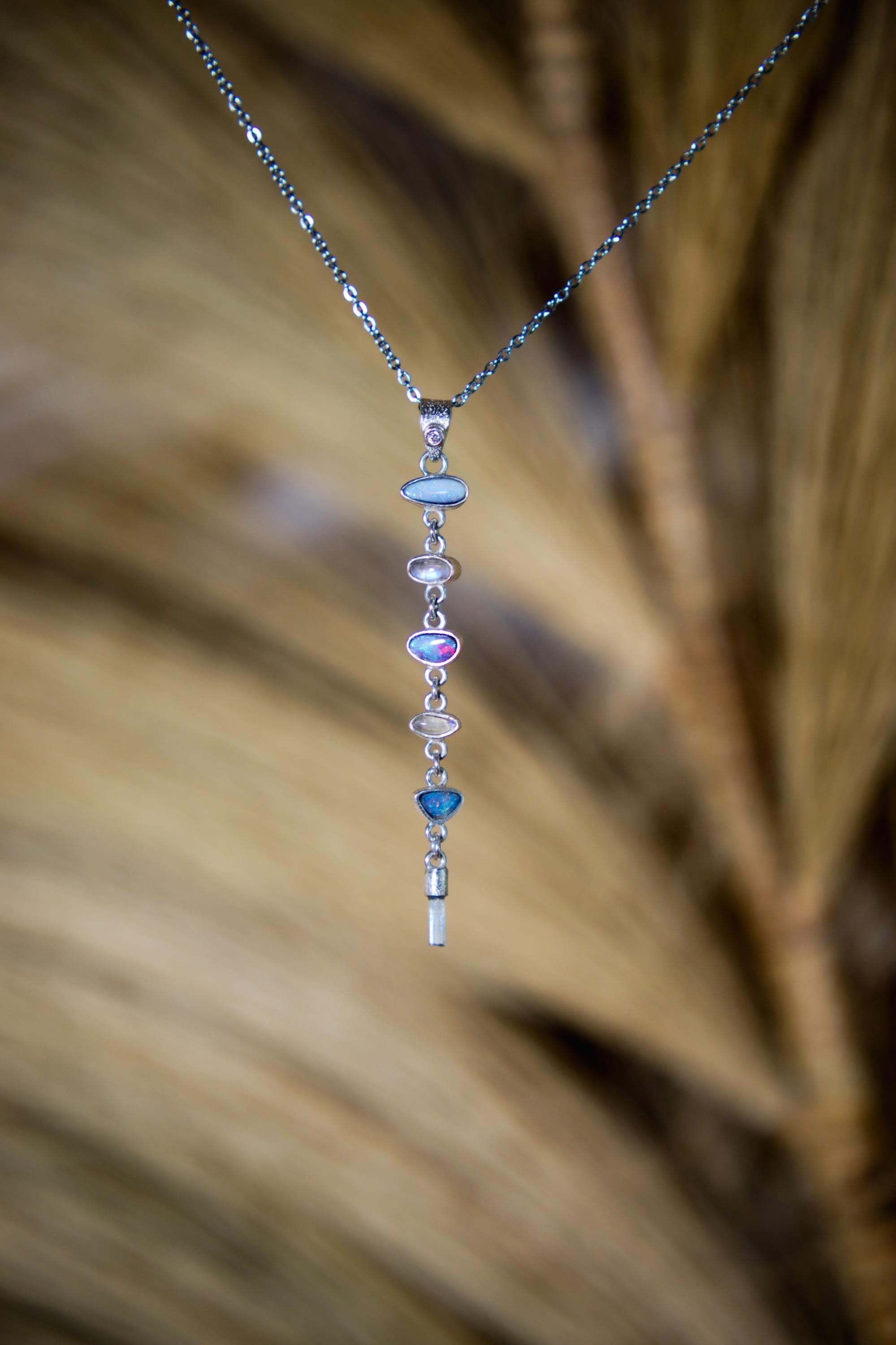 Faceted Zircon Opal Moonstone Aquamarine pendant shown against natural grass texture, with silver chain and blue-toned gemstone drop.