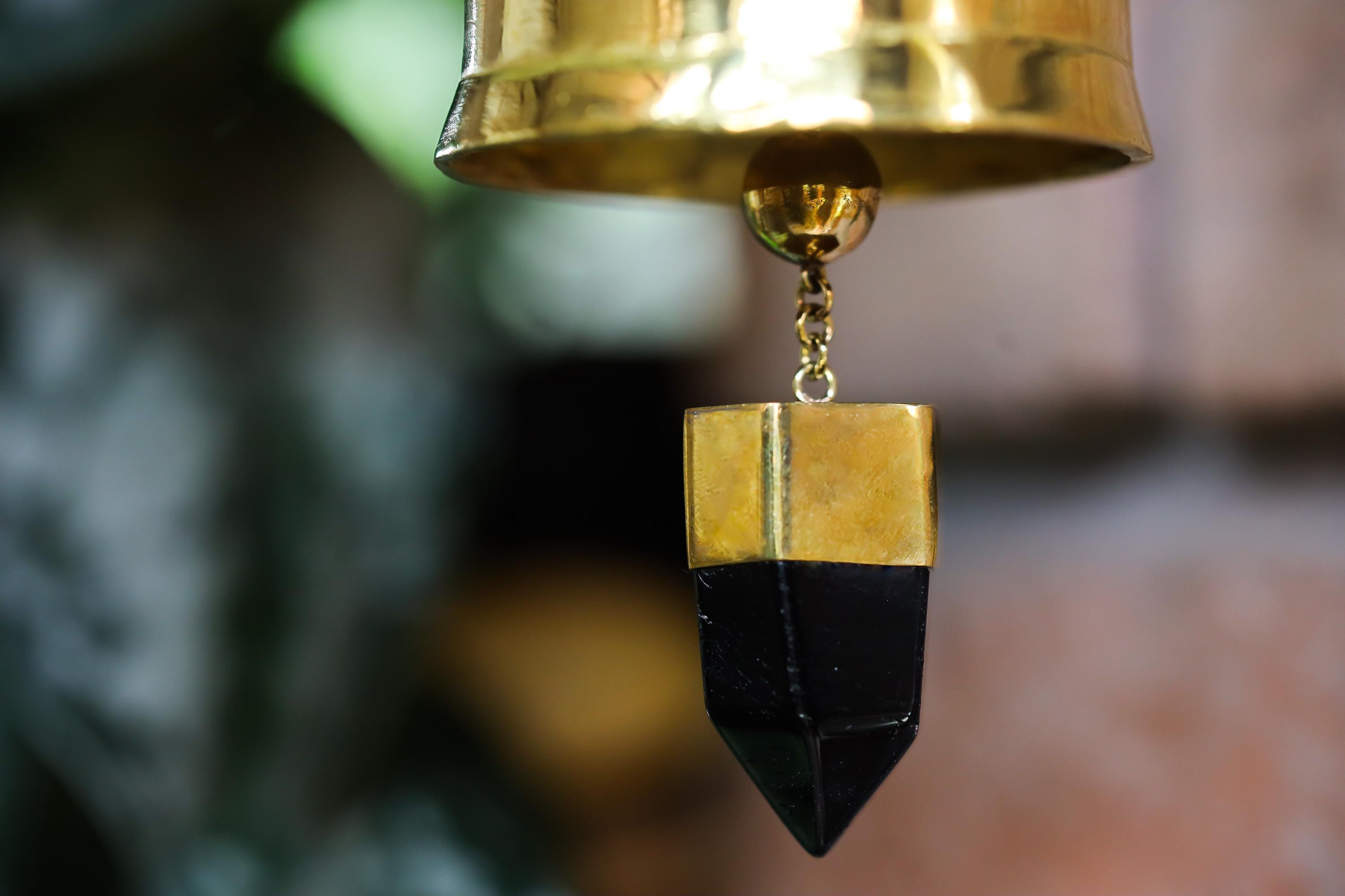 Close-up of Smoky Quartz point suspended inside gold-plated bronze prayer bell with dark crystal tip.