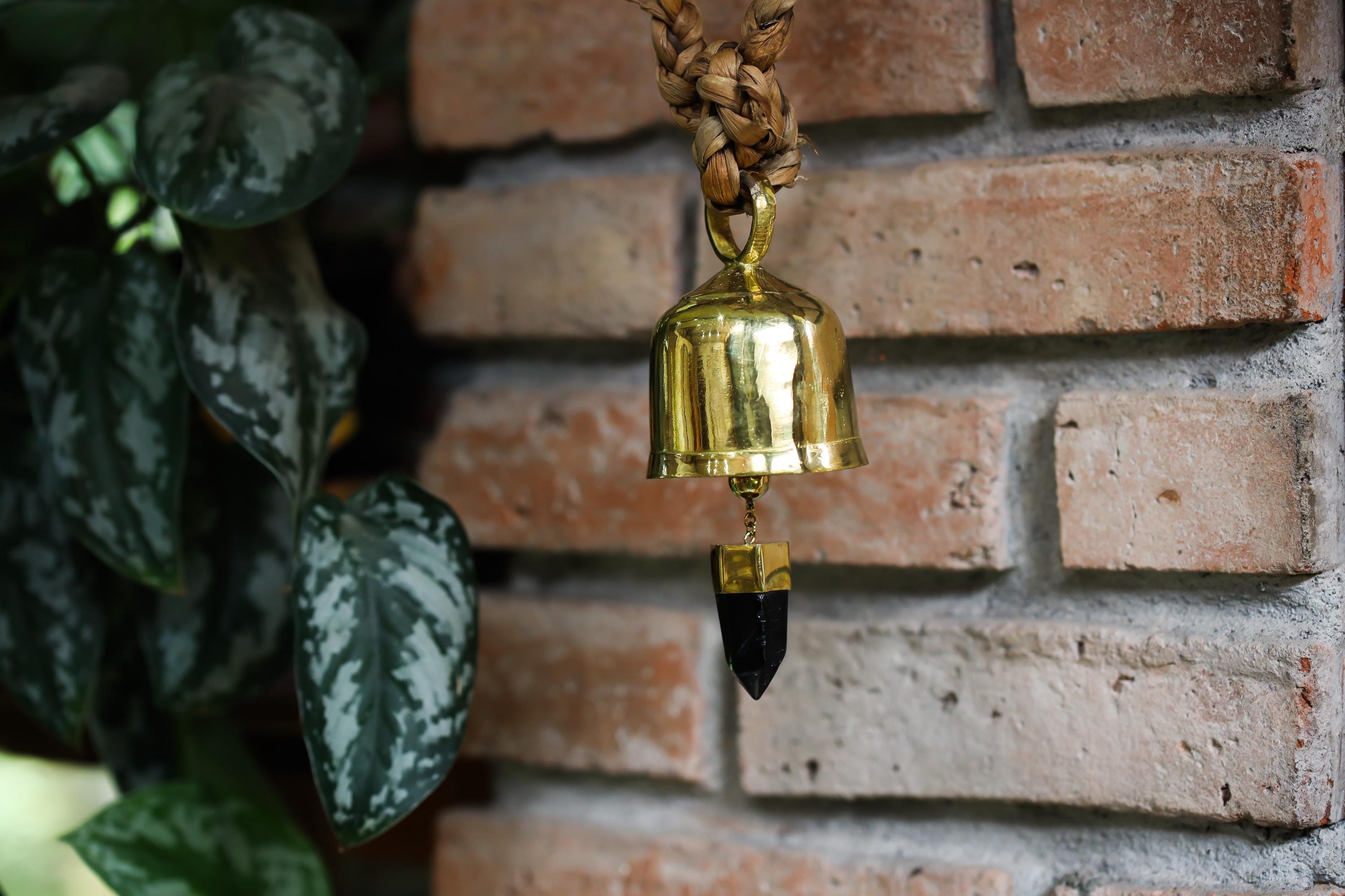 Smoky Quartz Gold Plated Prayer Bell hanging near plants and brick wall with ceremonial gold finish.